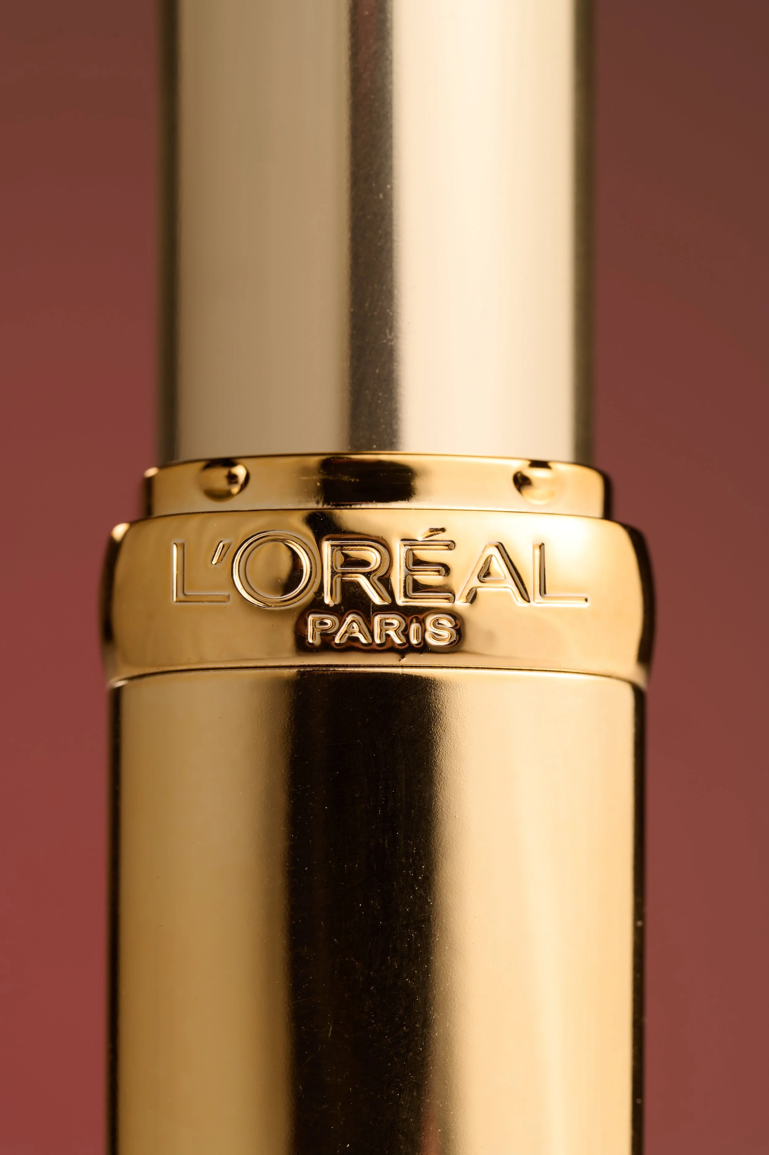 Close-up of a gold lipstick tube branded with L'Oréal Paris against a pink background.