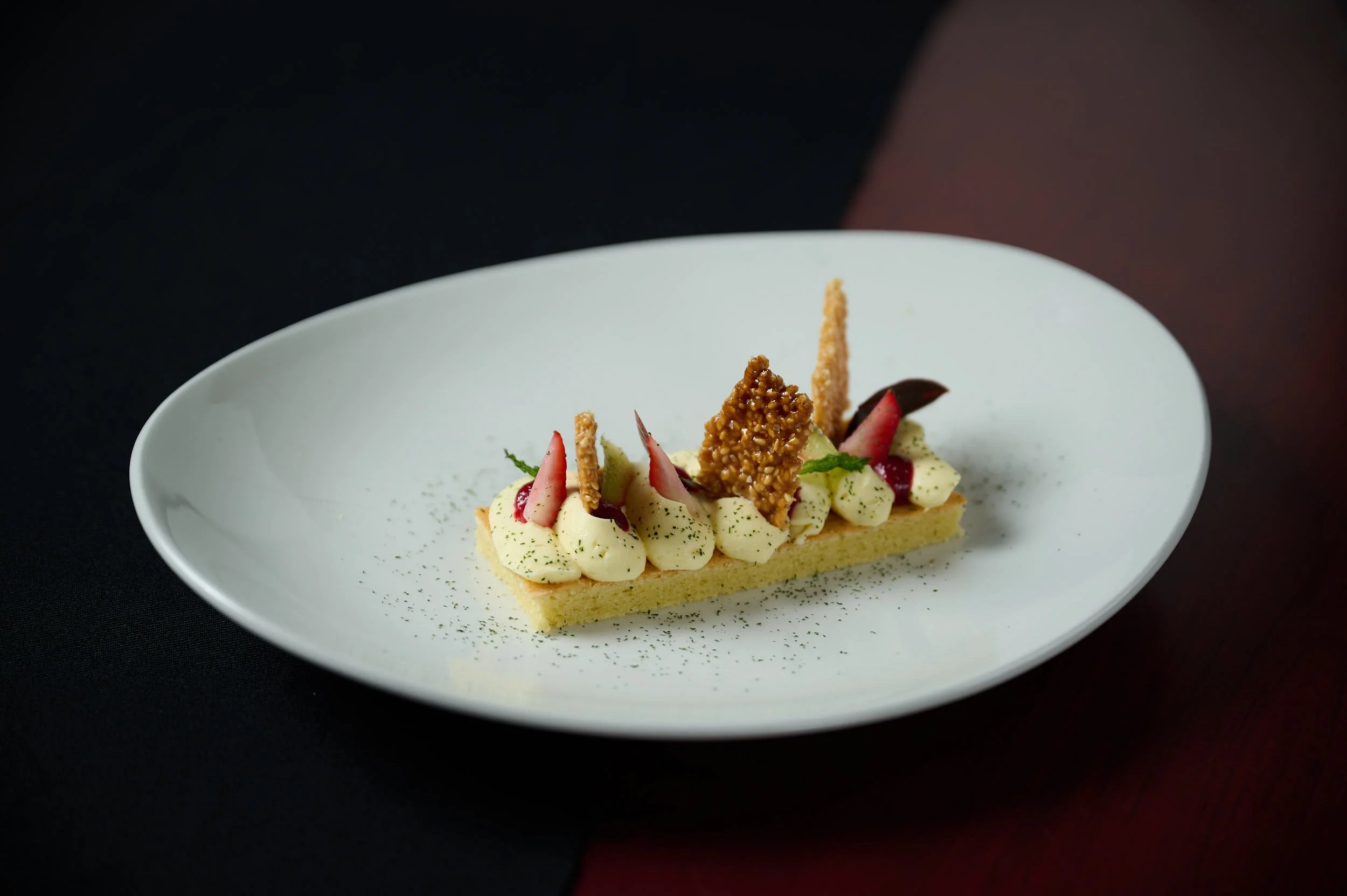 Elegant dessert with cream, fruit, and cookie garnishes on a white plate.