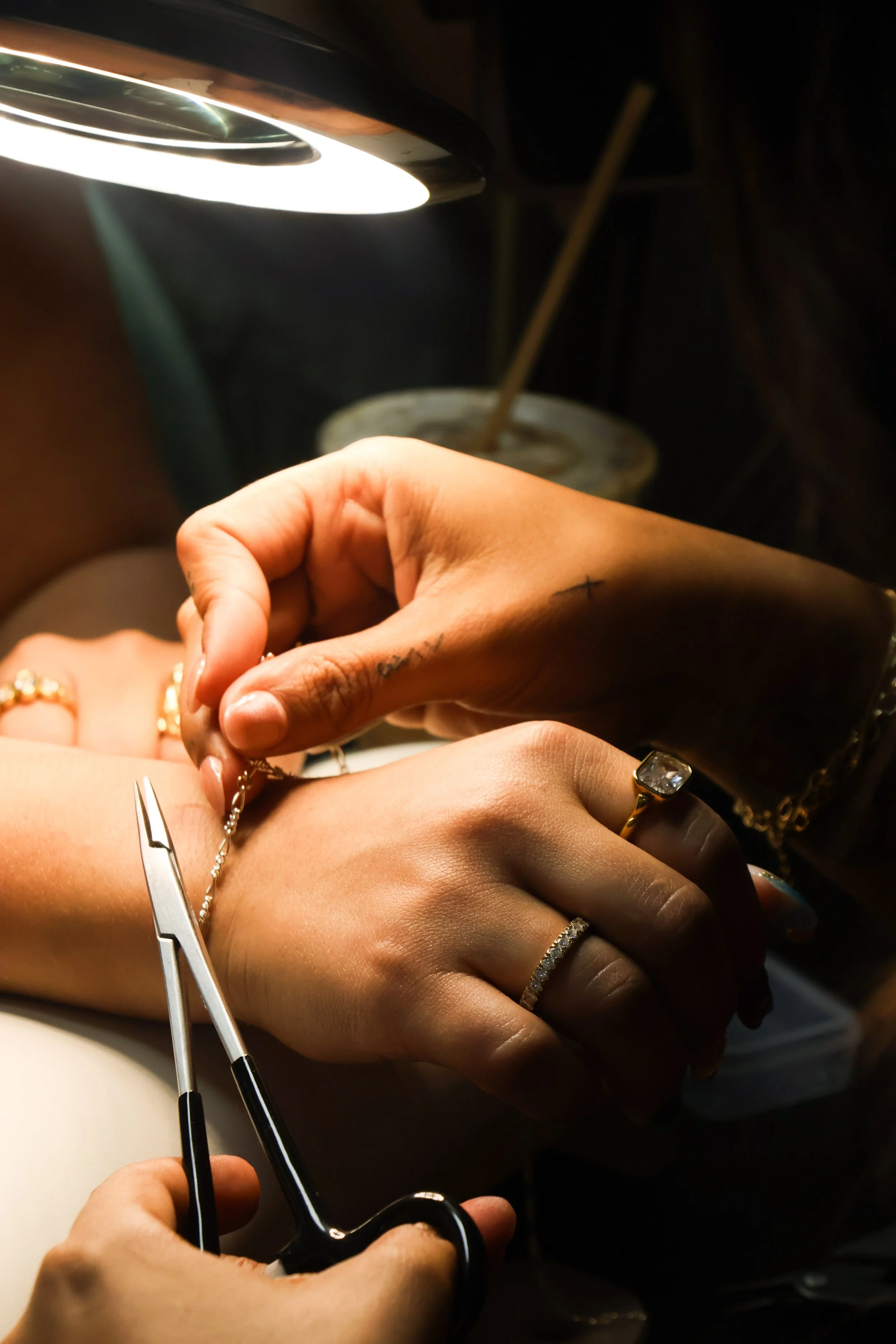 A hand holding a clear glass coupe with a jewelry stand inside it, displaying various gold and silver necklaces and bracelets against a plain white background.