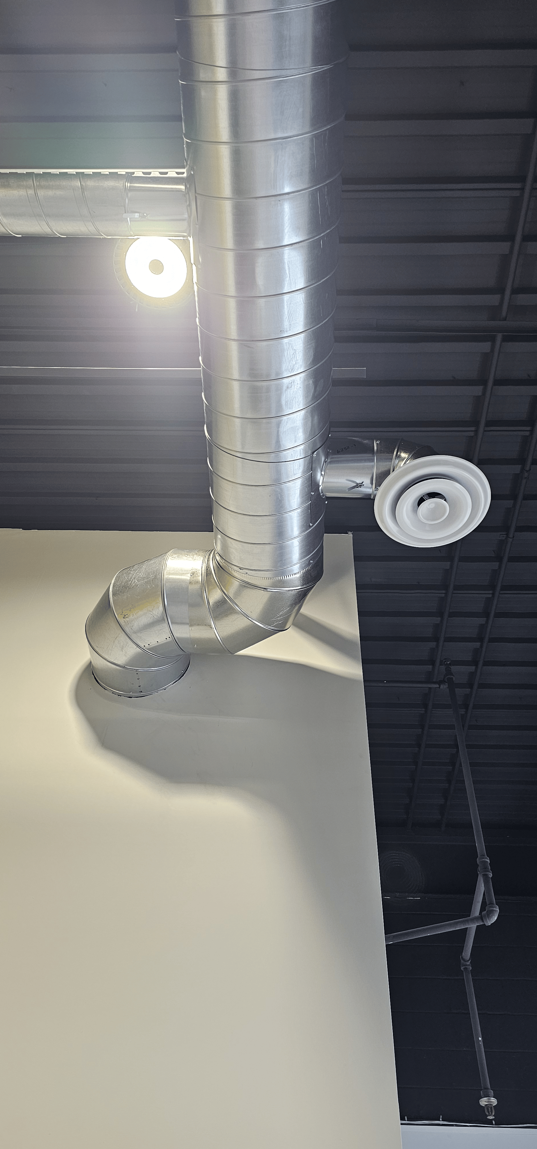 Industrial ceiling ventilation ducts and a white ceiling vent in a modern building interior.