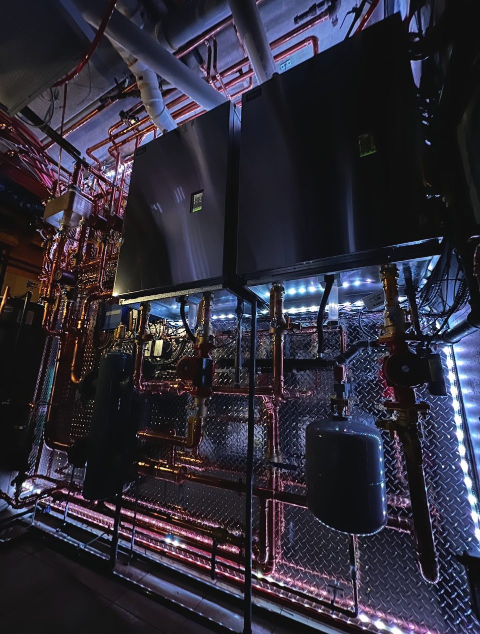 Industrial mechanical room with black equipment, copper pipes, and LED lights.