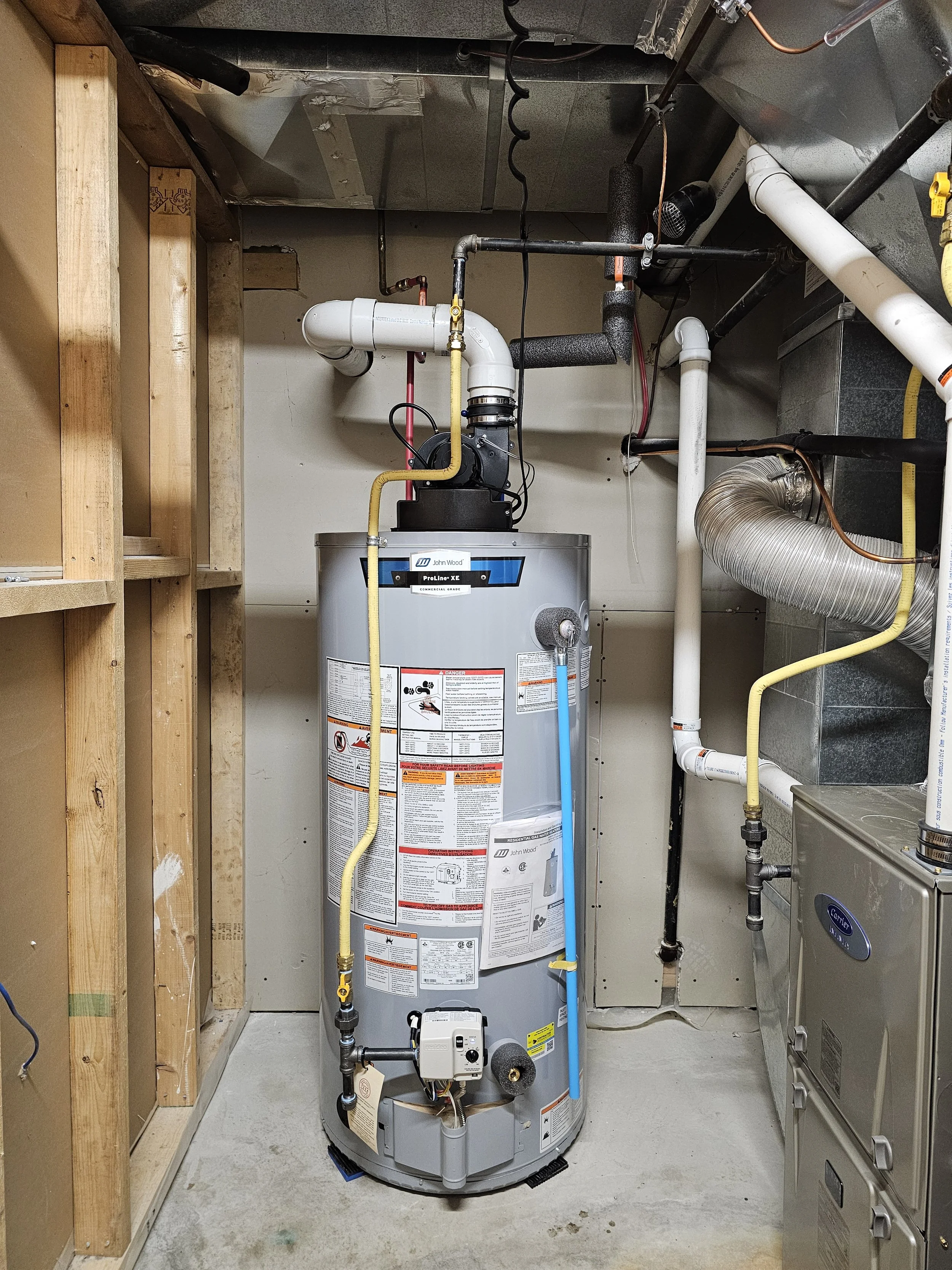 A new water heater installed in a utility room with exposed wooden framing on the left and ductwork and pipes on the right.