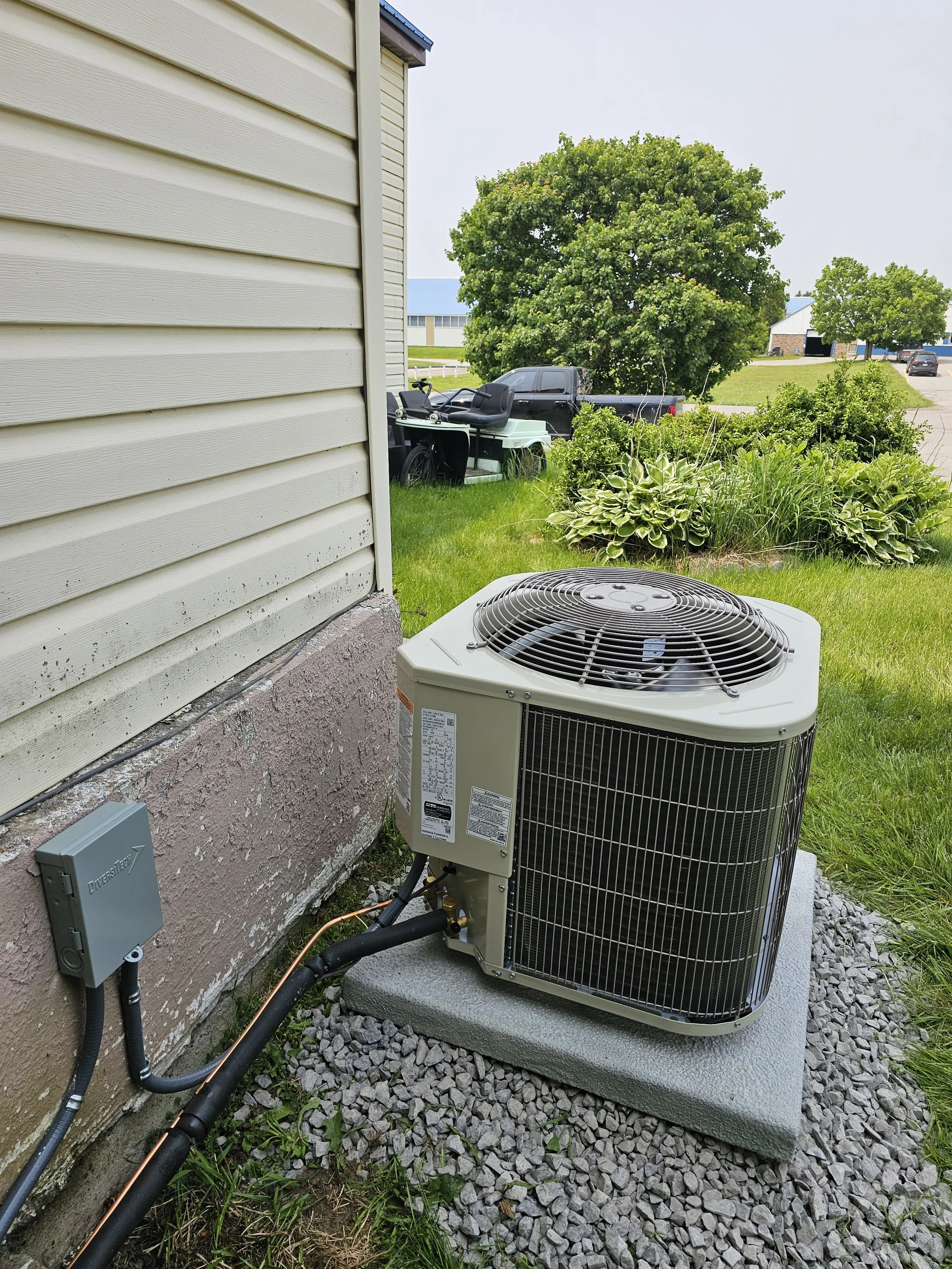 An outdoor HVAC unit installed next to the side of a house with beige vinyl siding, situated on gravel ground.