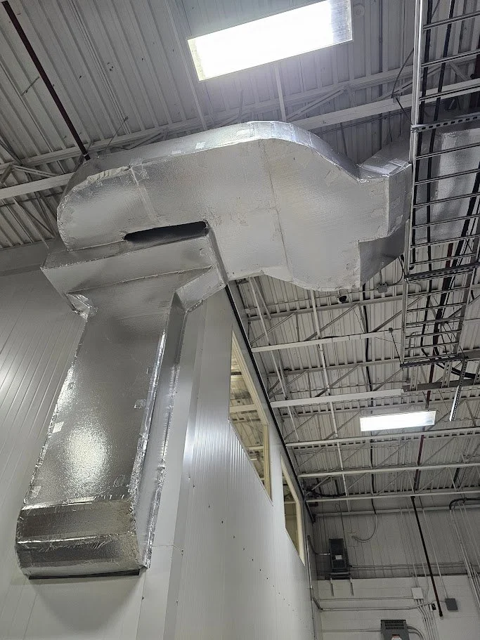 Large metallic air duct installed on the ceiling of an industrial building.