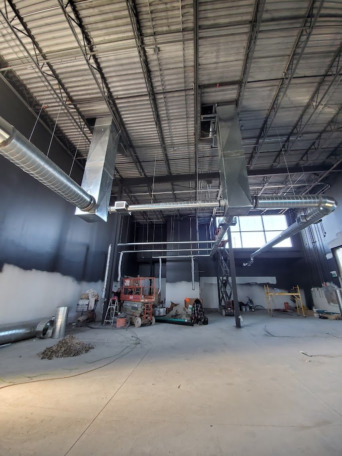 Construction inside a large industrial building with exposed ductwork, scaffolding, and building materials.