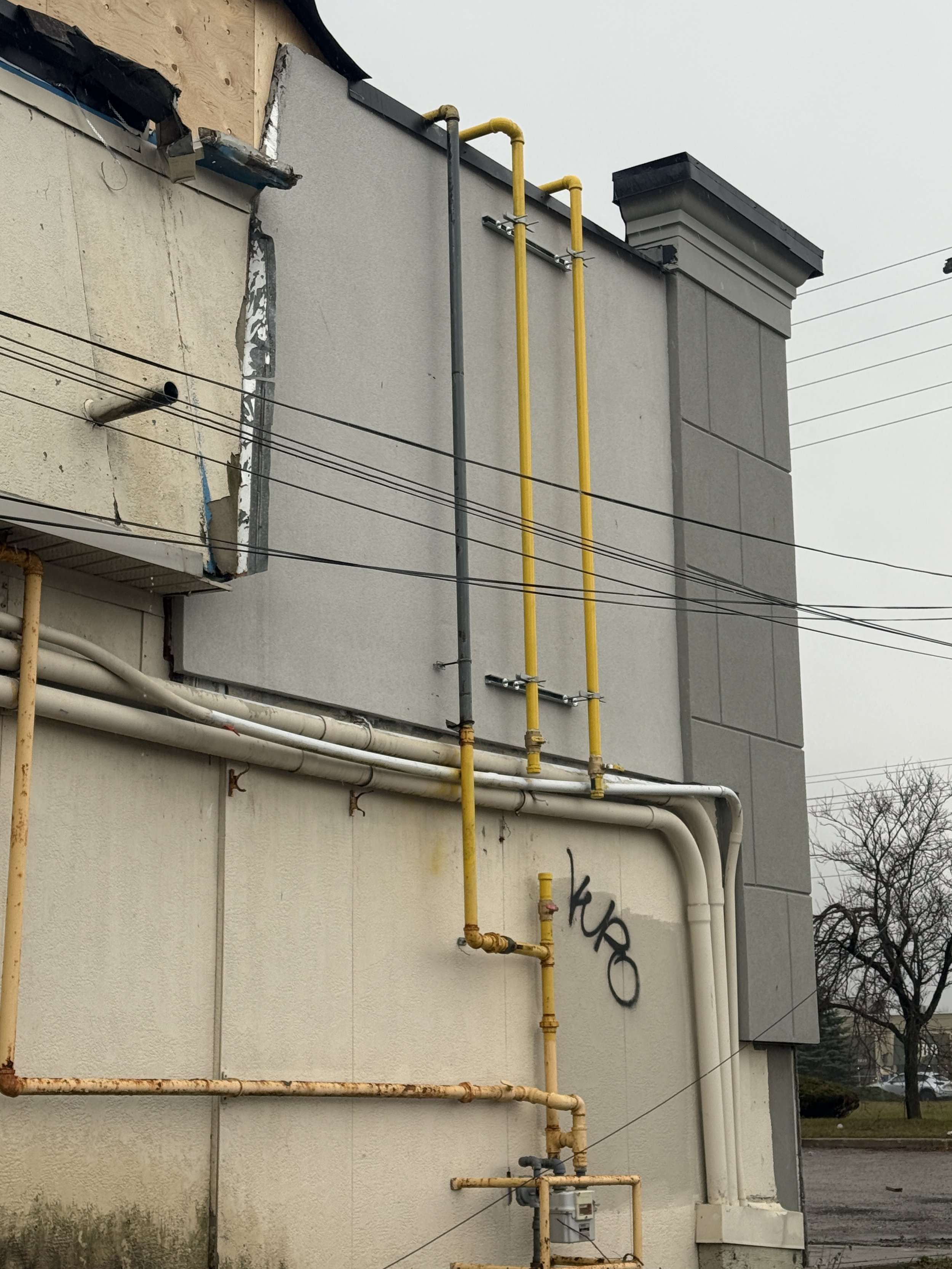 Close-up of a building's exterior wall showing yellow and white pipes, with some graffiti, and the sky in the background.