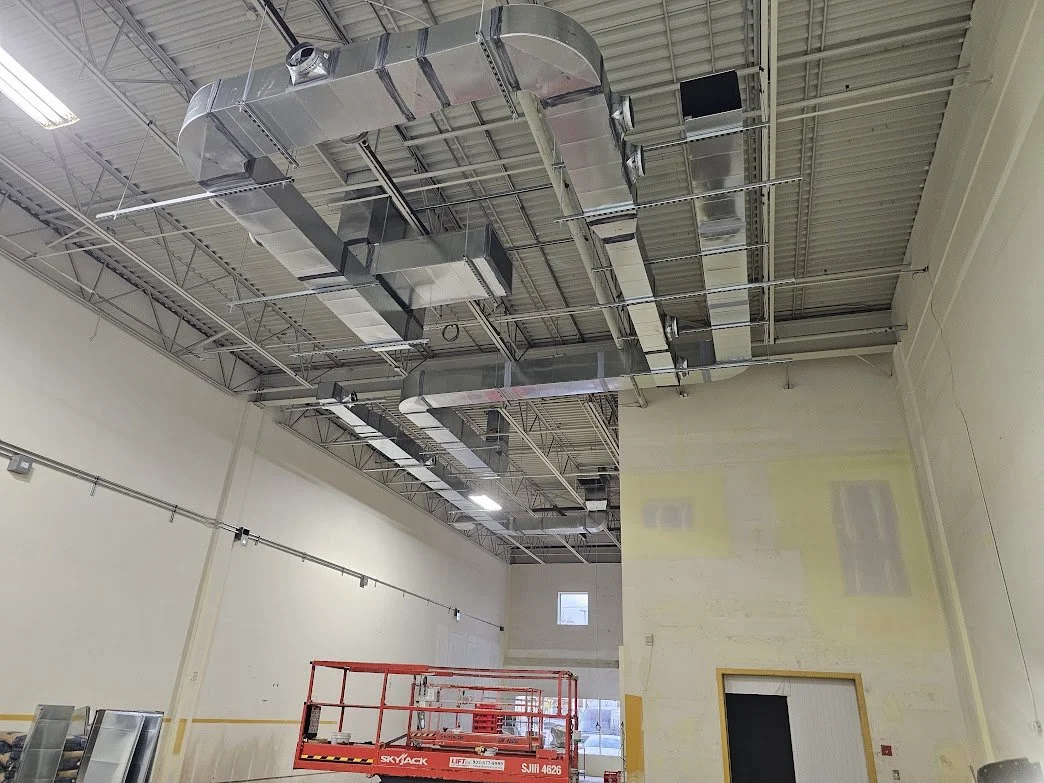 Interior of a commercial building under construction with exposed ductwork and a scissor lift.