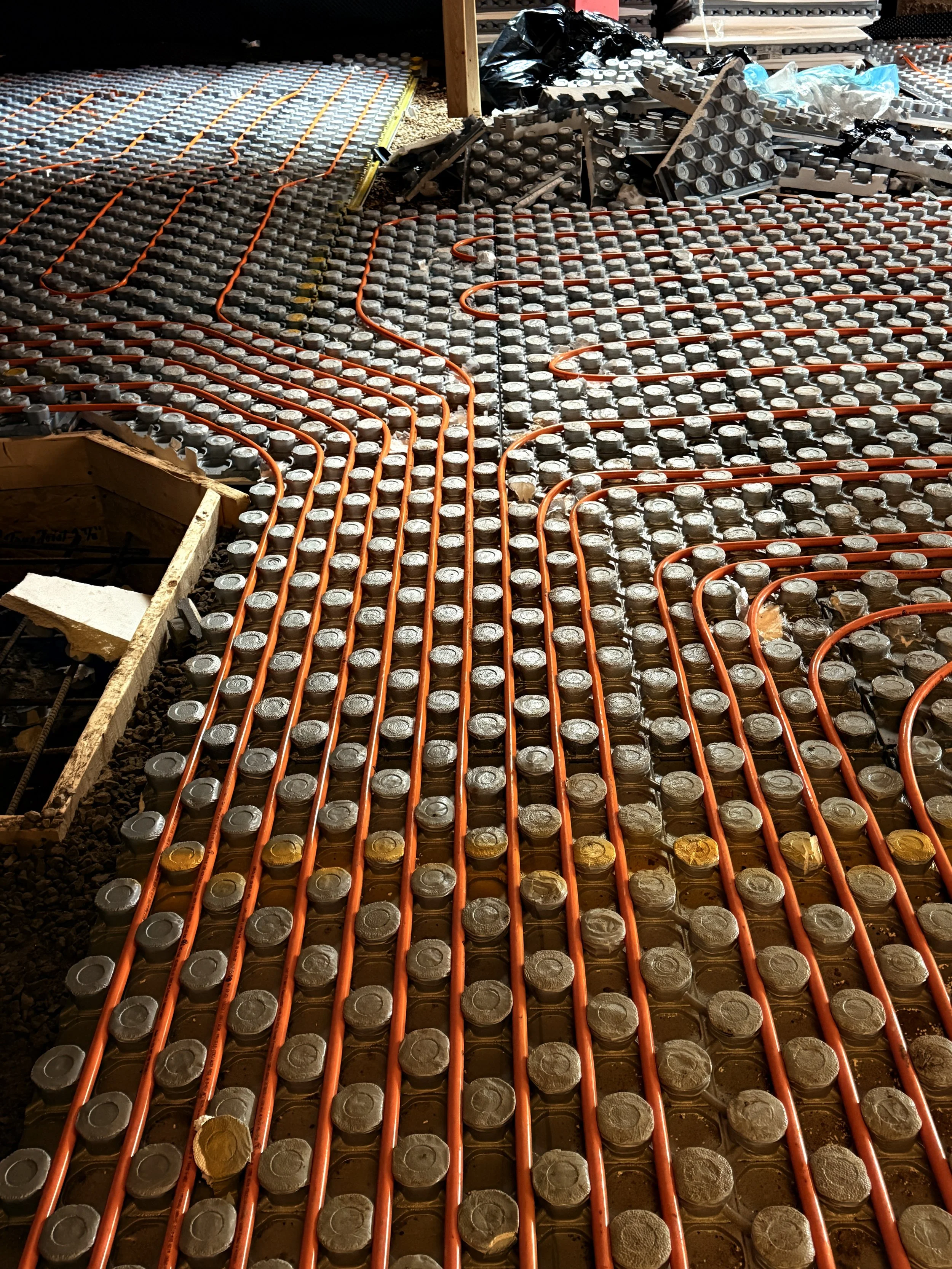 Underfloor heating system installation with orange pipes laid over metal plates in a construction site.