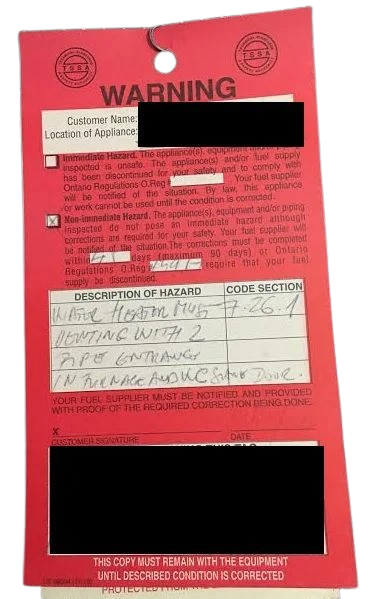 Warning tag with red background and checkboxes, handwritten notes, and a redacted customer name.