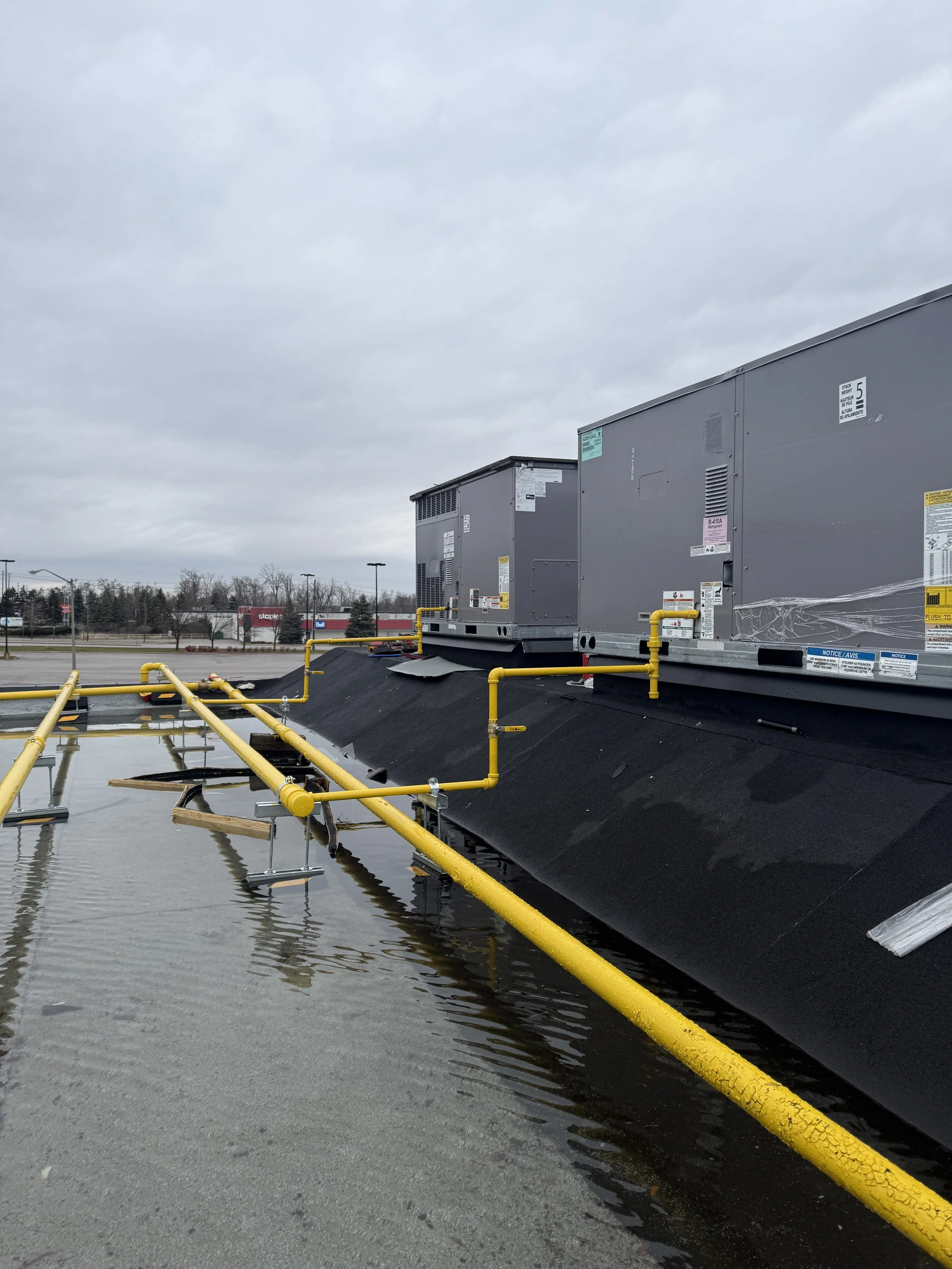 HVAC units on a rooftop above water with yellow pipes and overcast sky.