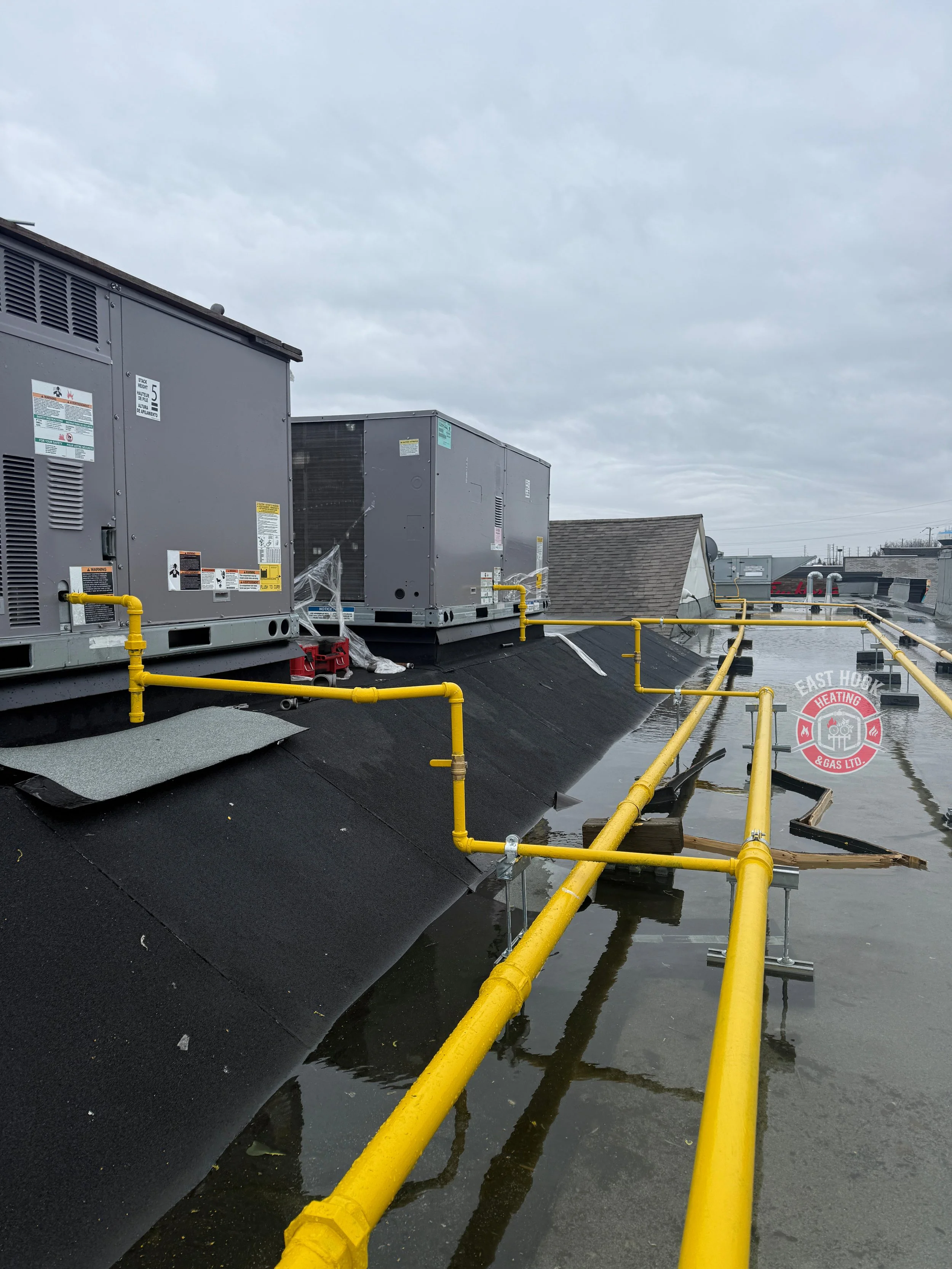 Roof with industrial HVAC units and yellow gas pipes, with water accumulation on the surface.