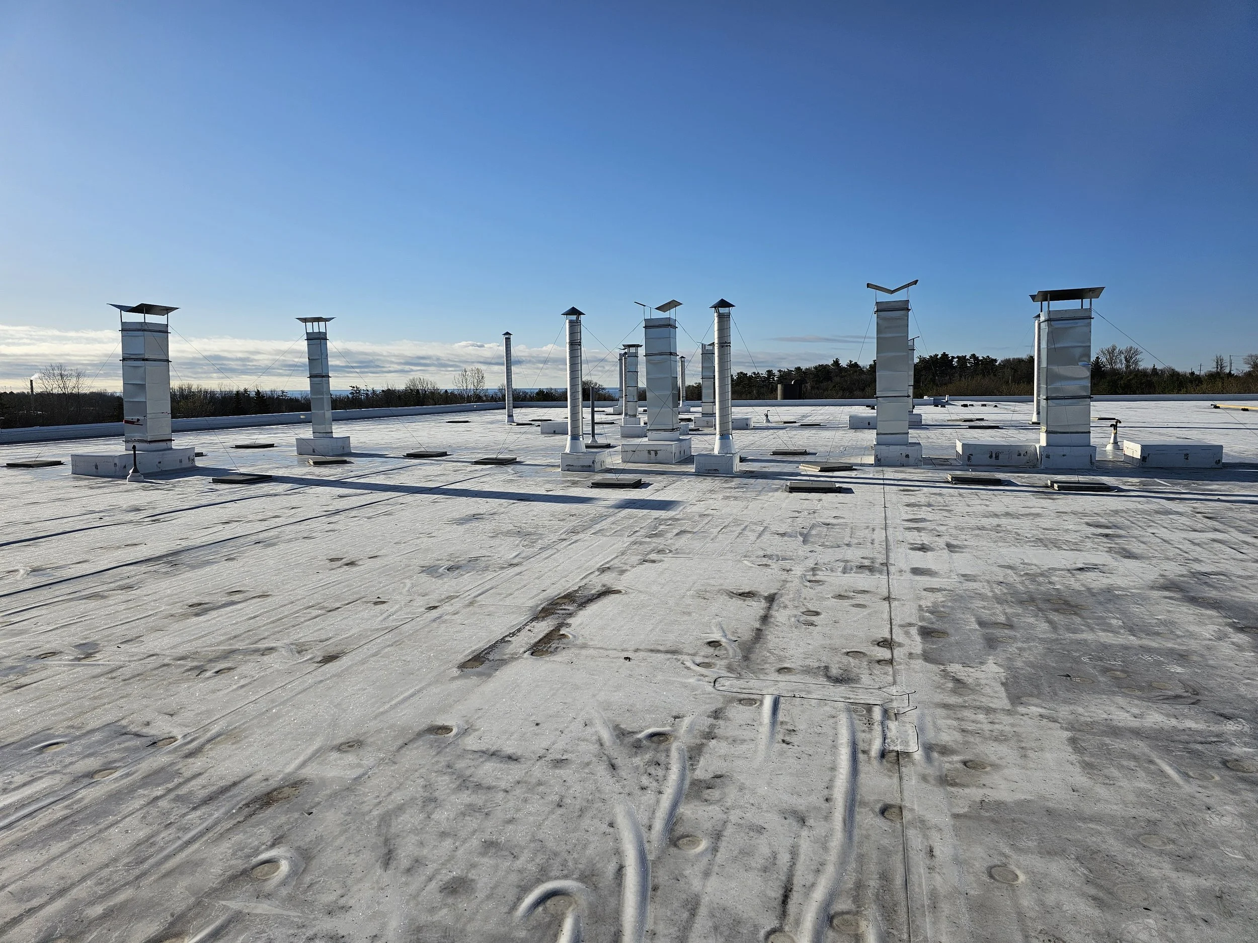 Rooftop with multiple ventilation ducts and electrical conduits under a clear blue sky.