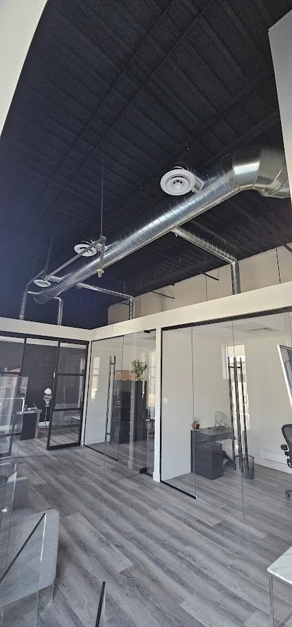 Modern office space with glass walls, industrial ceiling, and exposed ductwork.