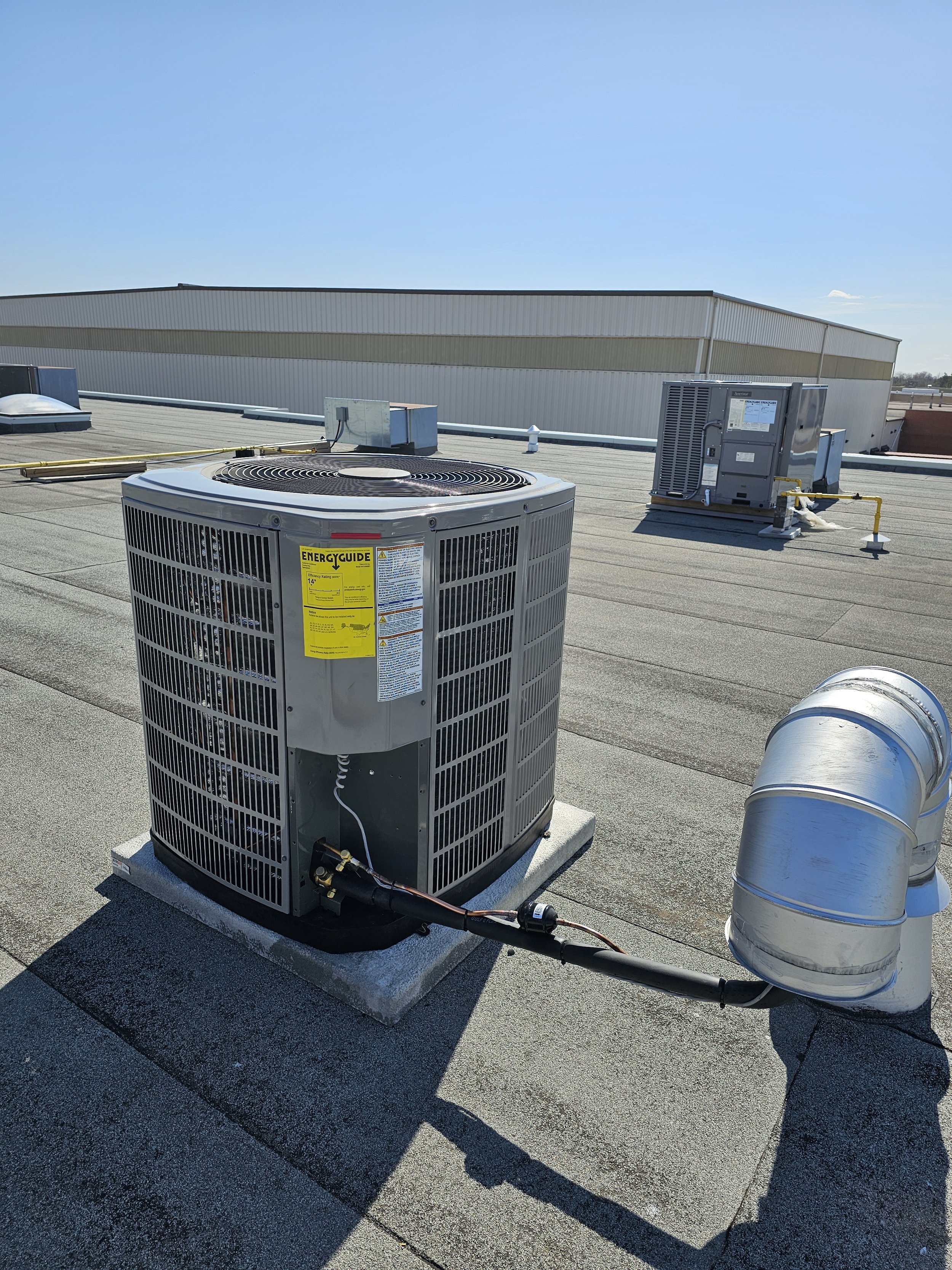 Rooftop HVAC units and ductwork on a flat roof under a clear blue sky.
