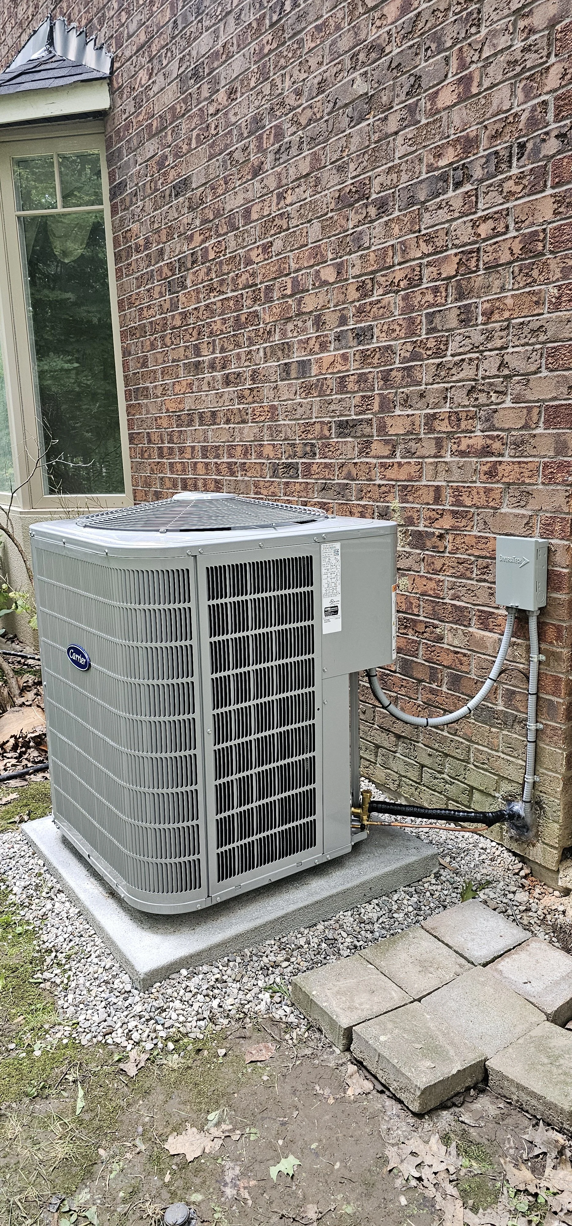 Outdoor view of a Carrier HVAC unit installed on a concrete pad beside a brick house wall.