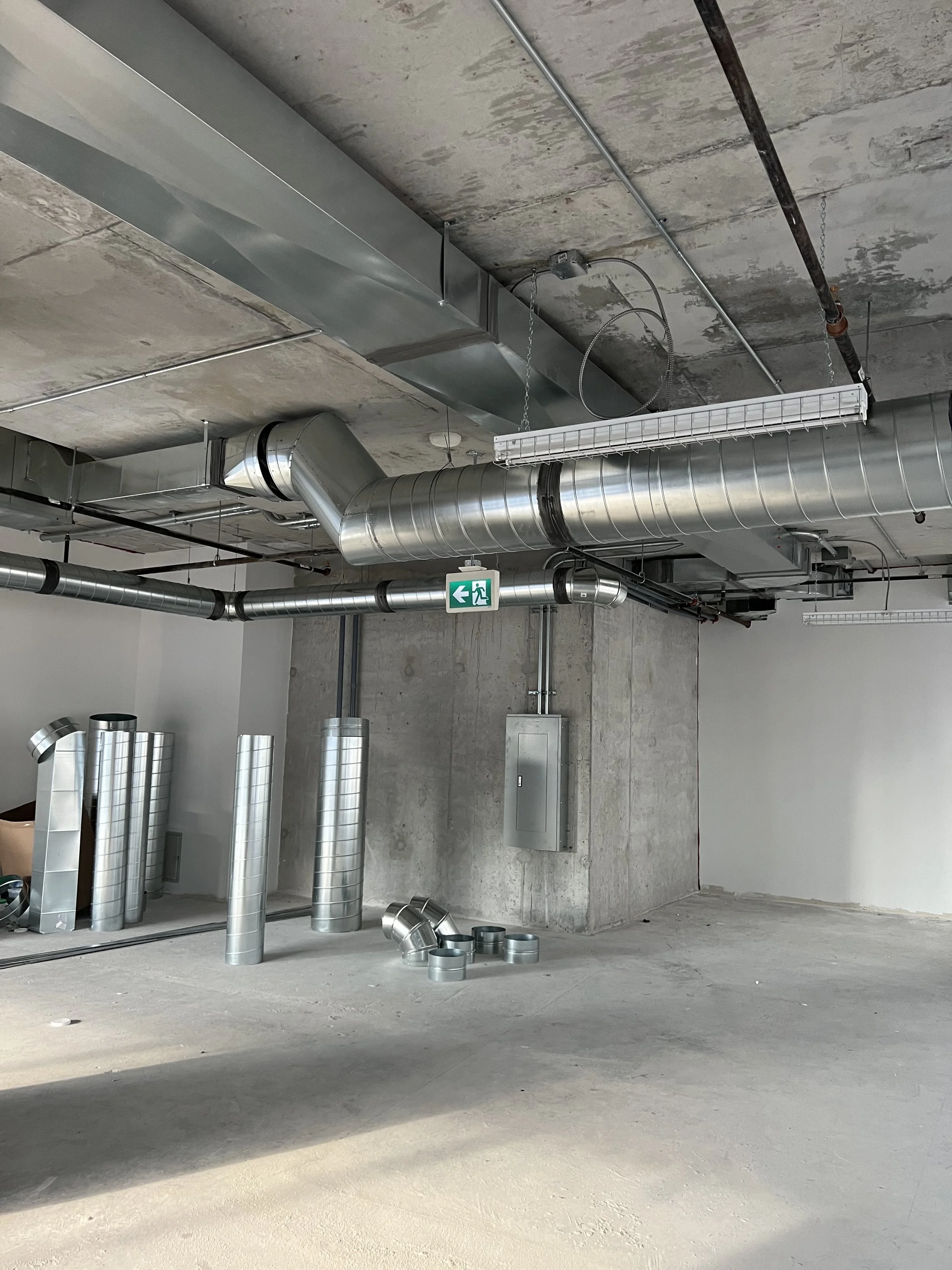 Construction site with exposed ductwork, electrical panel, and concrete walls and ceiling.