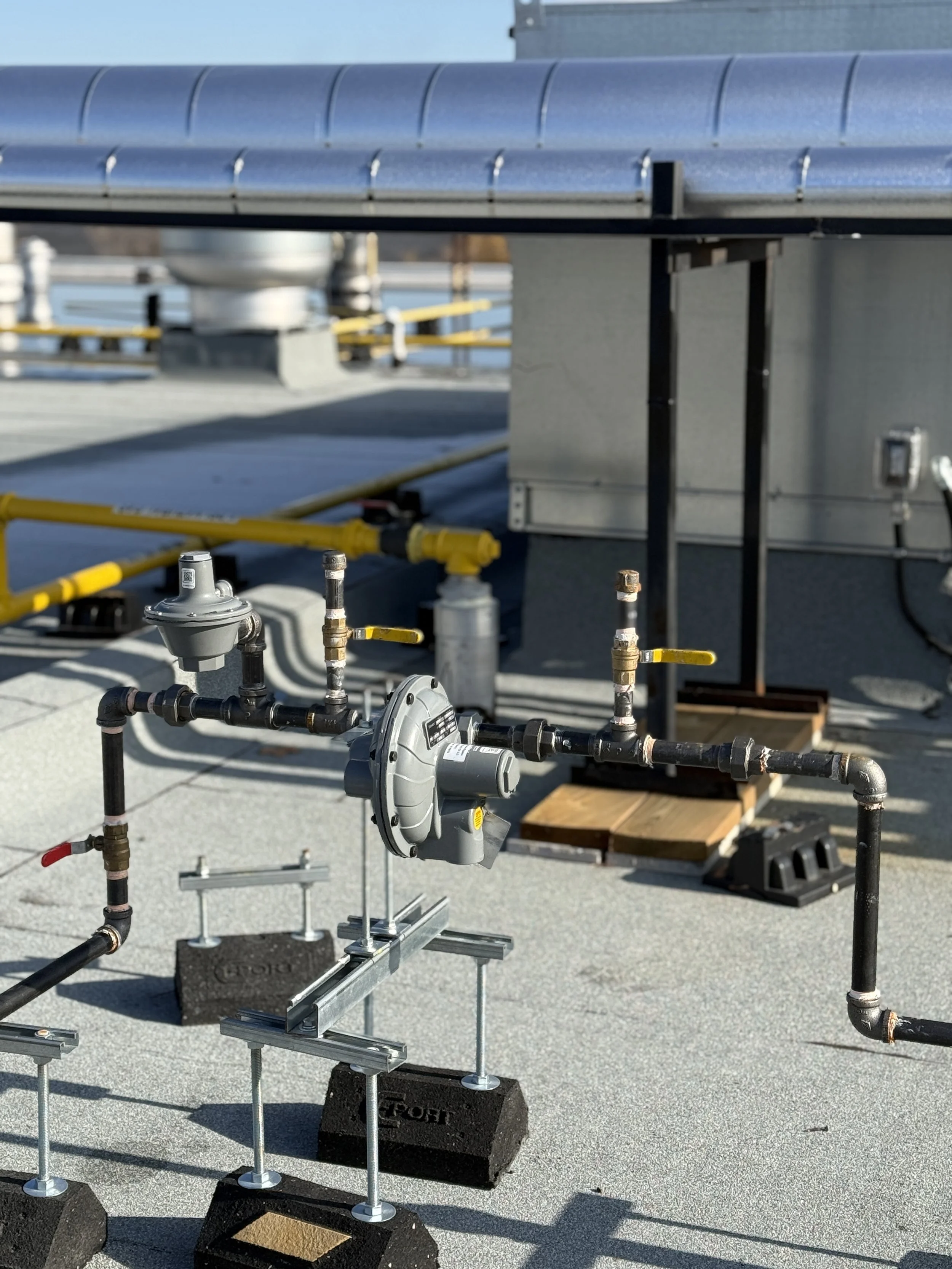 Rooftop HVAC or utility equipment with pipes, gauges, and controls on a flat roof.