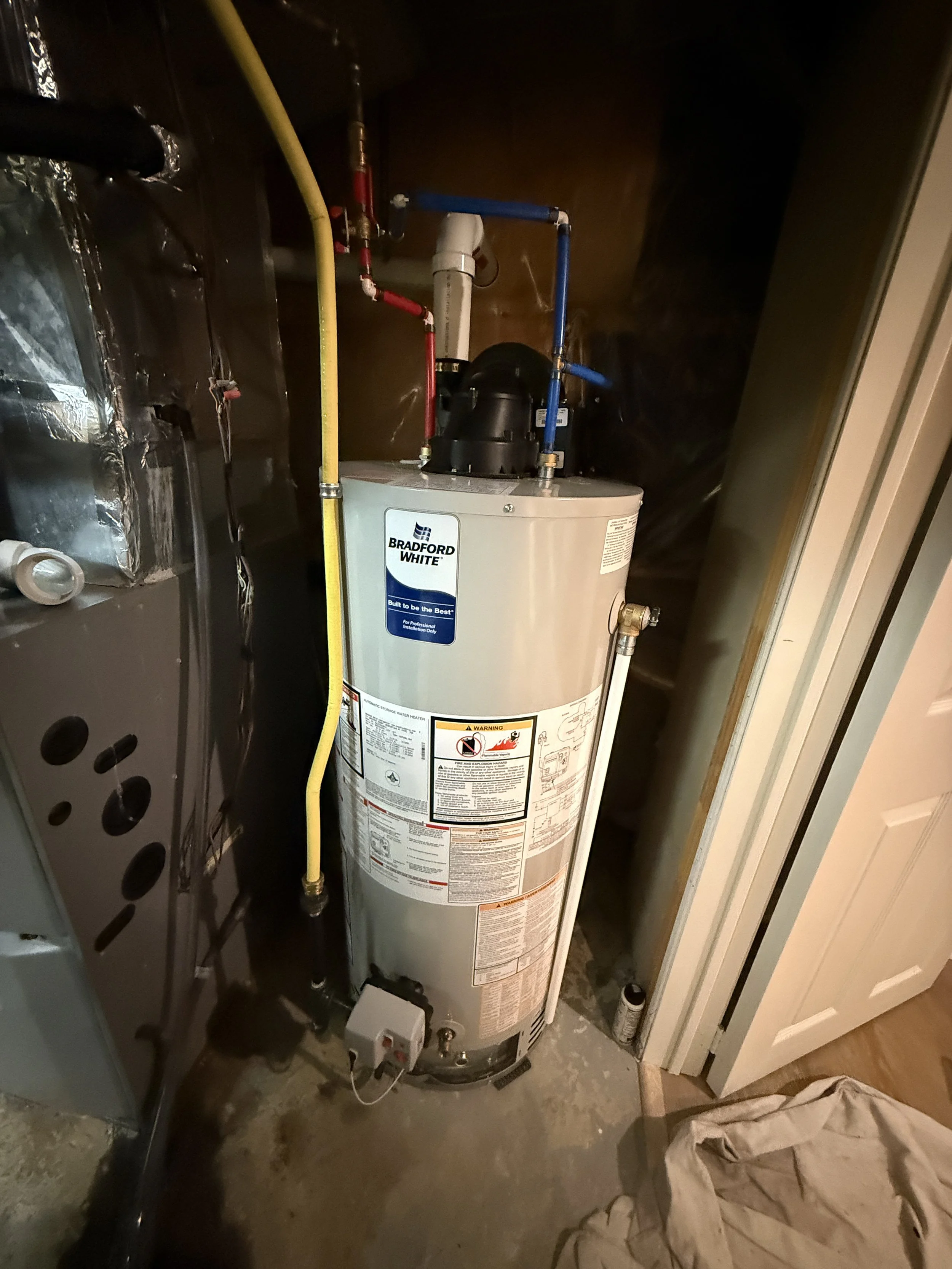 A Bradford White water heater installed in a utility closet with plumbing and electrical connections.