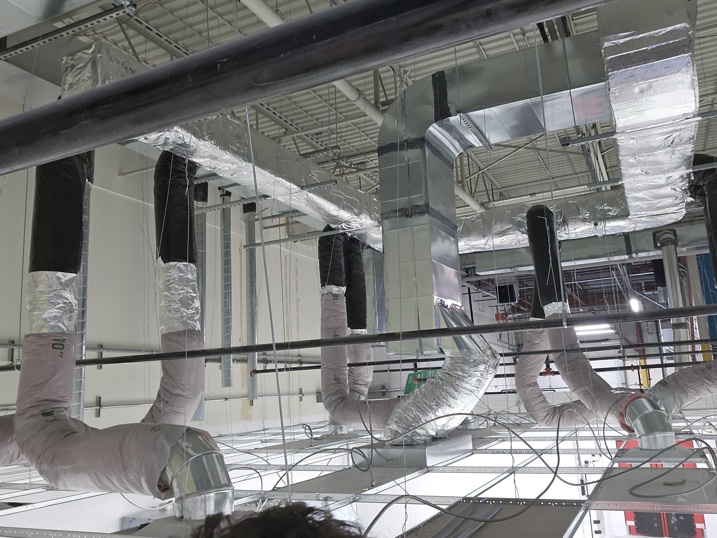 Ceiling with HVAC ducts, insulation, and electrical wiring in a commercial building construction site.