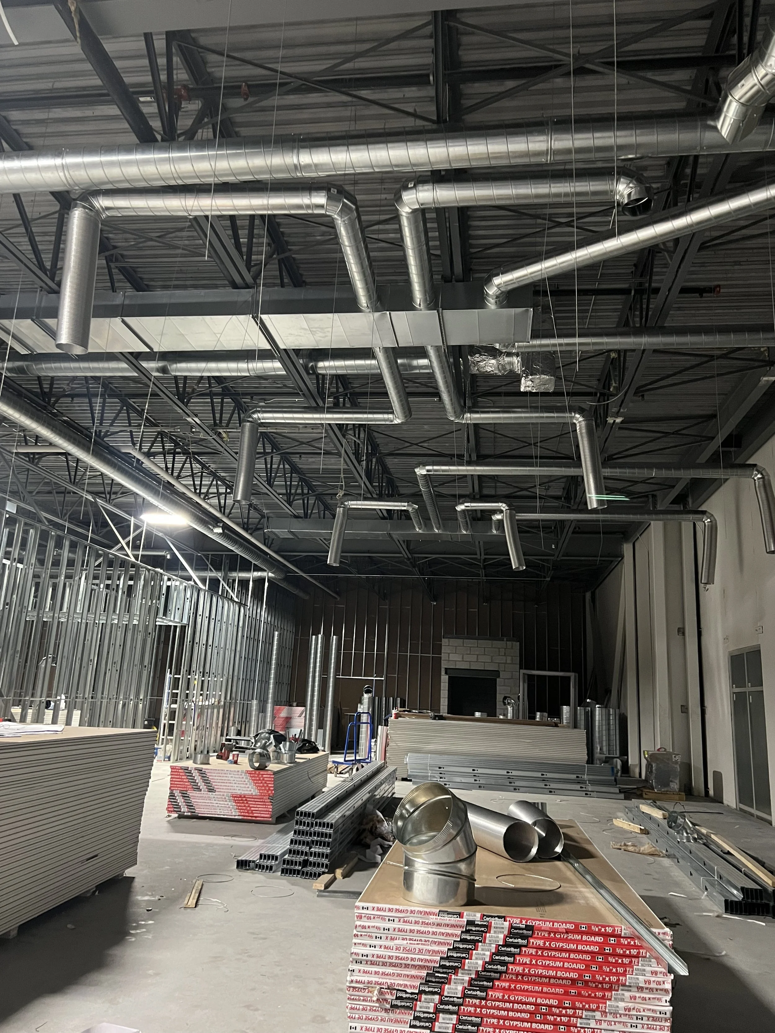 Construction site with exposed metal ductwork and framing, scattered construction materials, and unfinished interior walls.