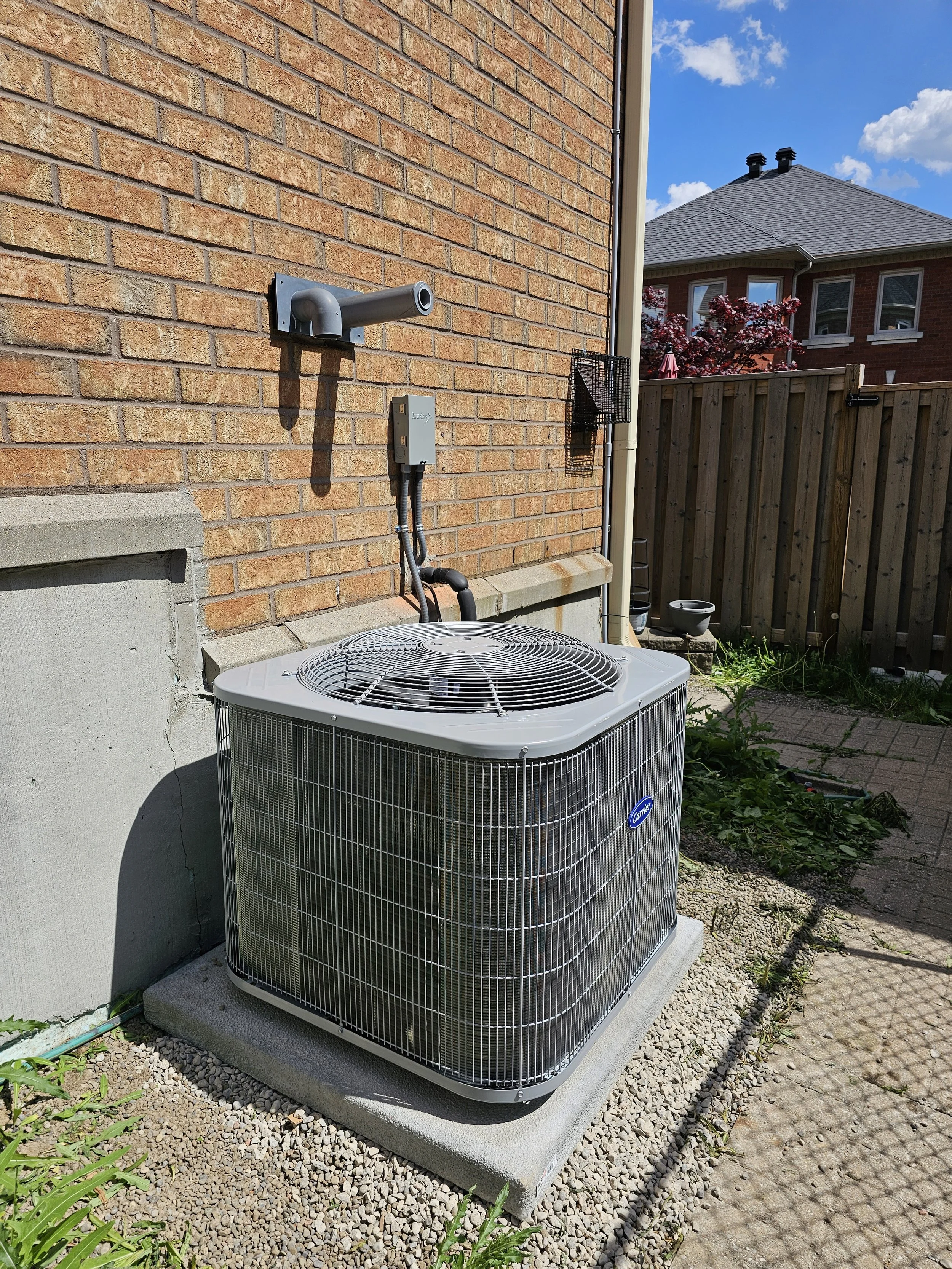 An outdoor air conditioning unit on a concrete pad next to a brick house wall.