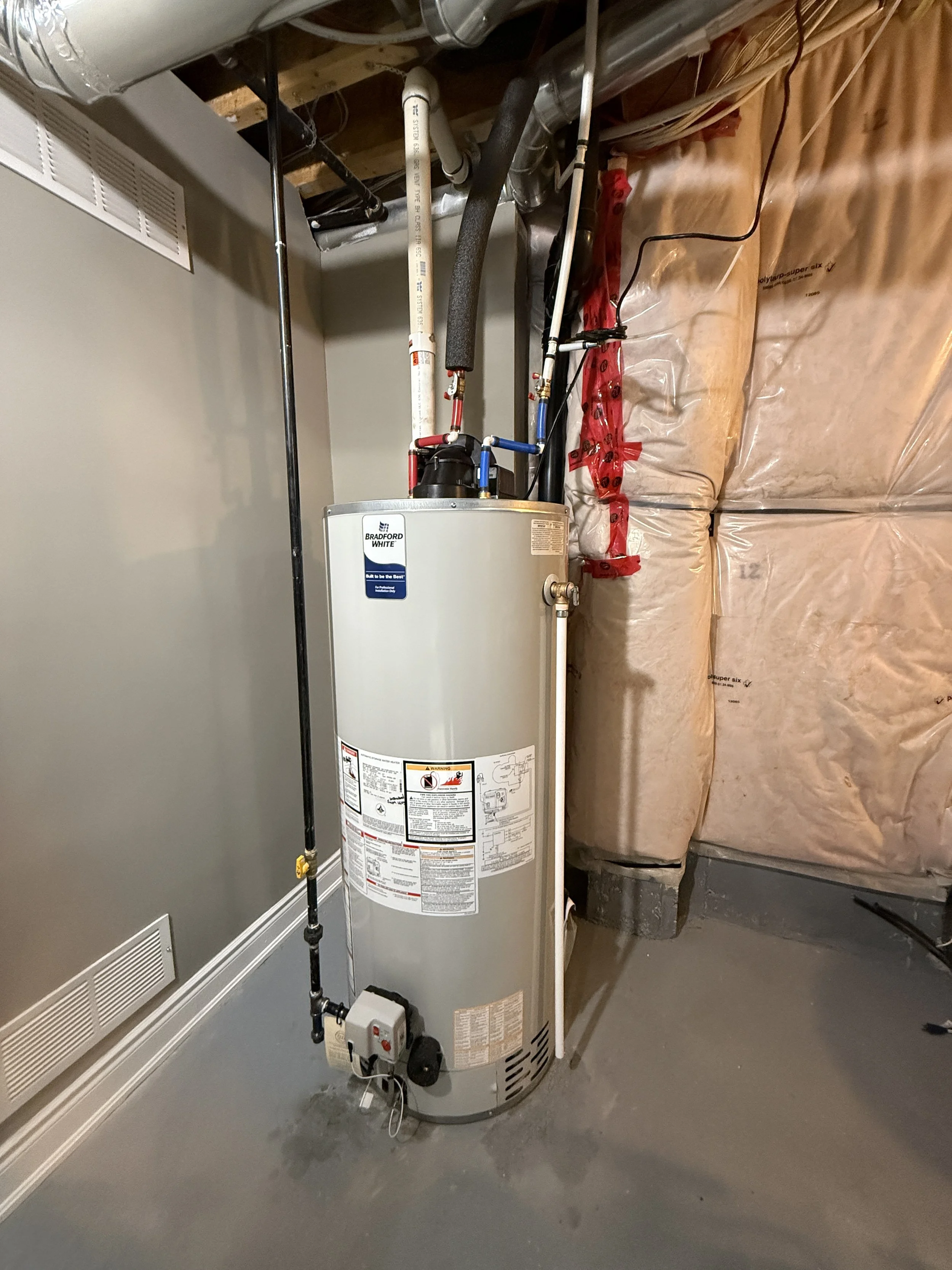 A water heater in a utility room with pipes and insulation around the walls.