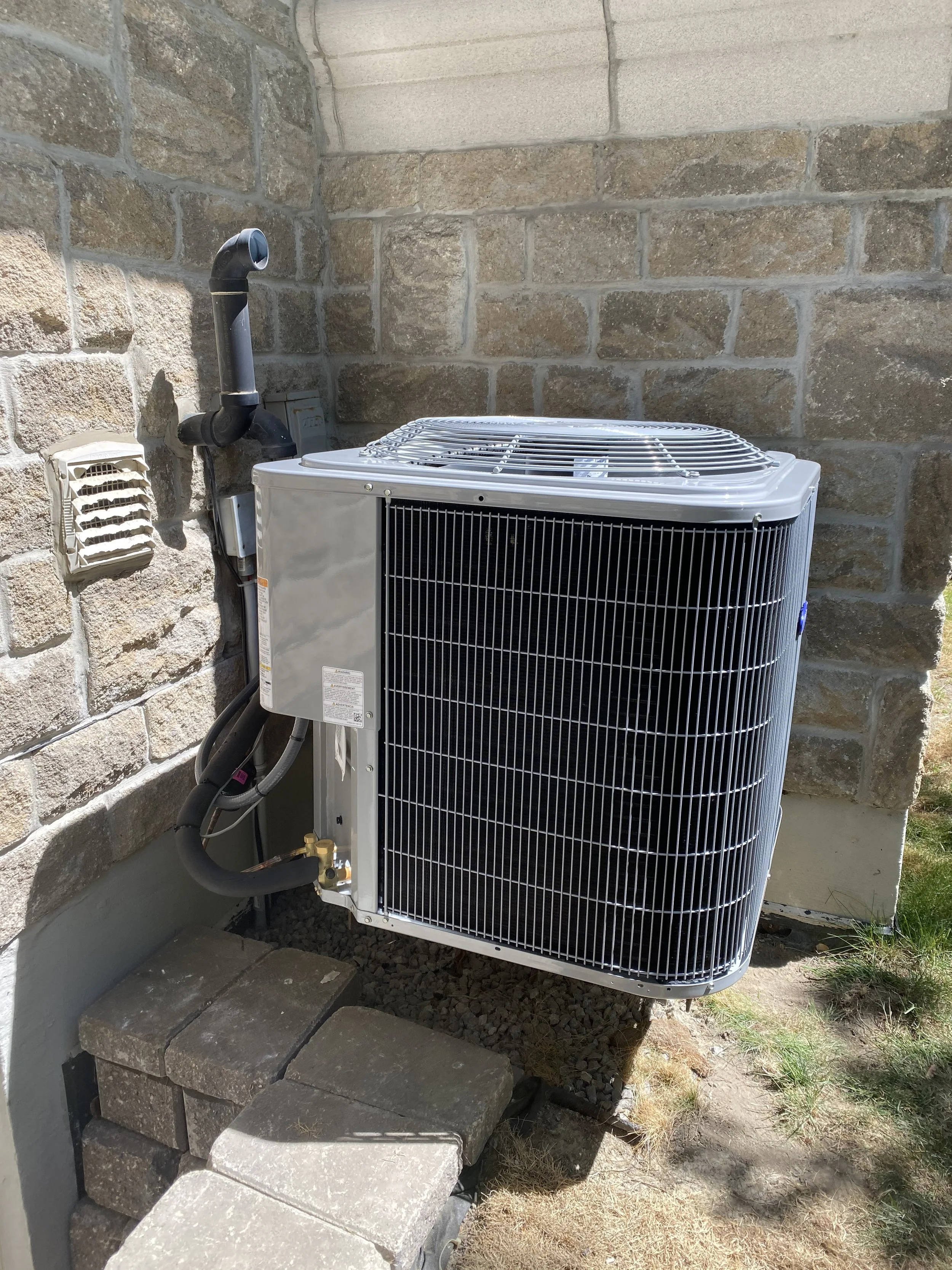 Outside air conditioning unit installed on a concrete pad next to the exterior wall of a house made of stone bricks.