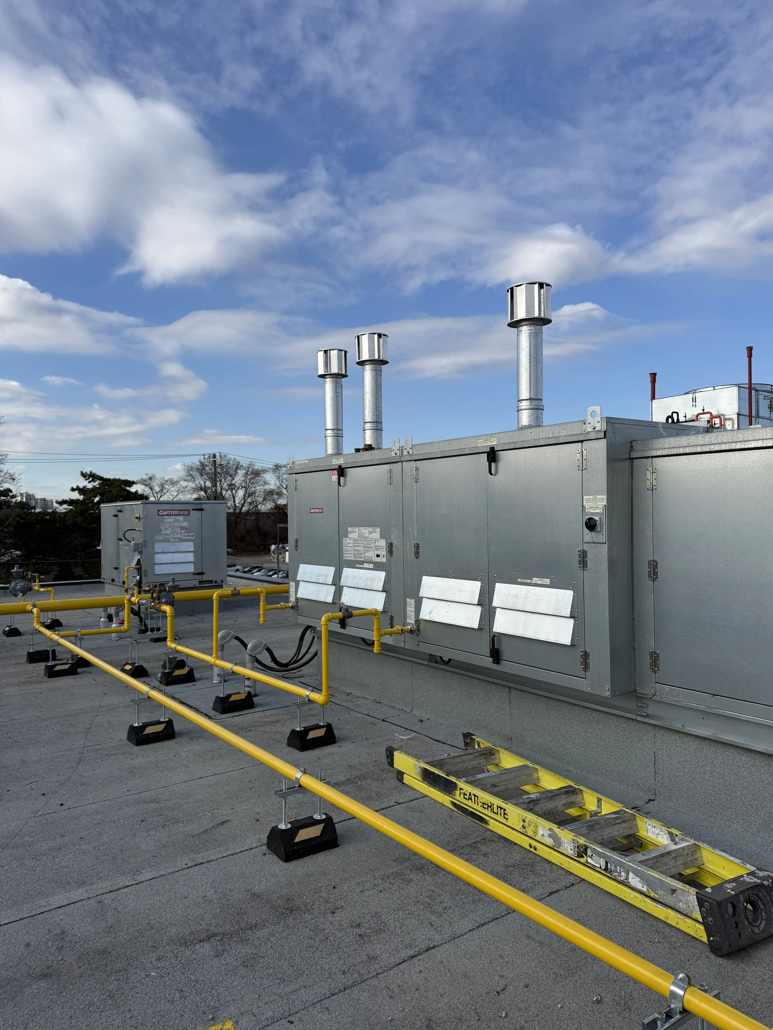 Industrial rooftop with HVAC units and yellow safety barriers, cloudy blue sky in background.