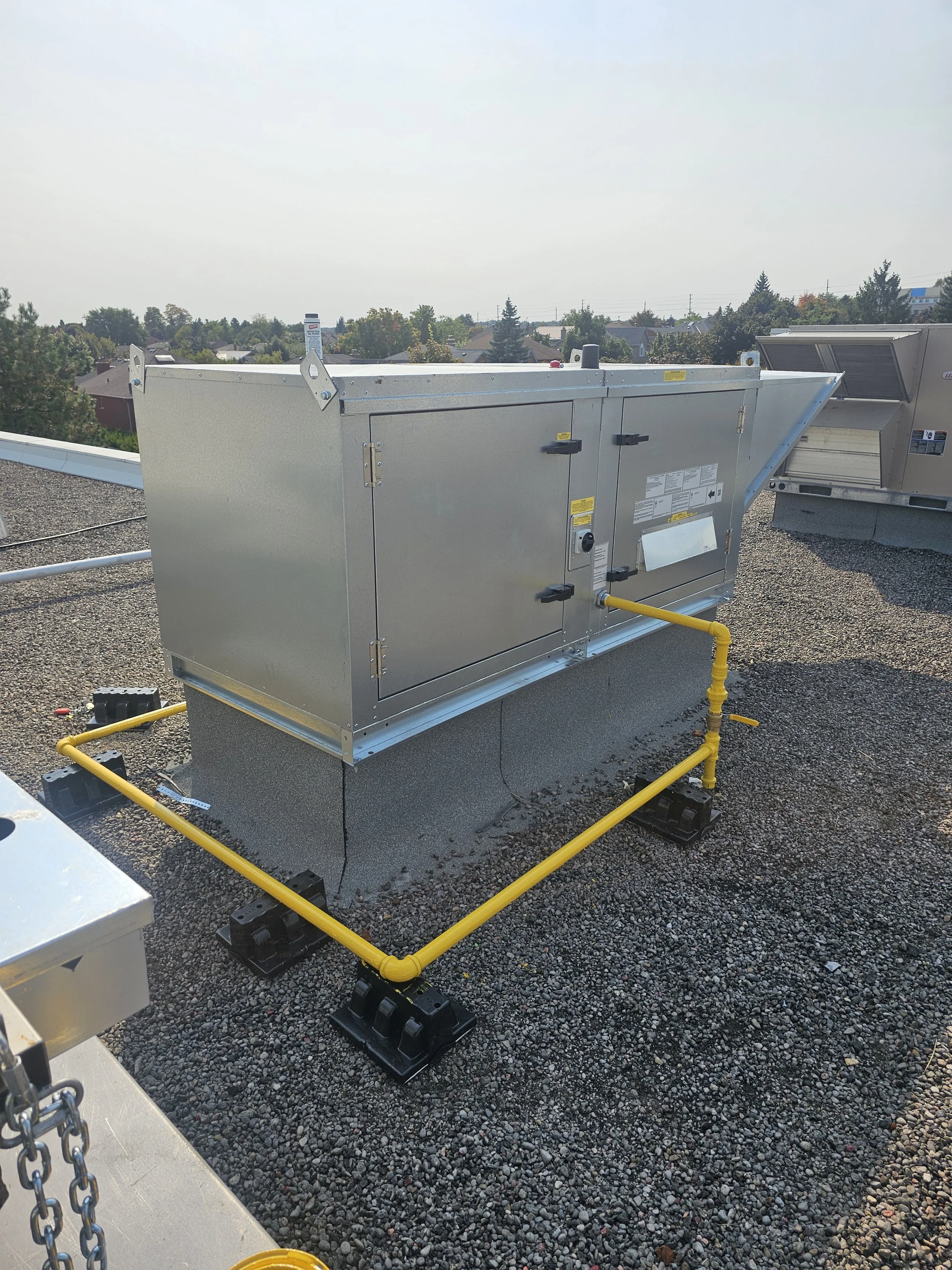 HVAC rooftop unit installed on a building with yellow gas line and seal bases on gravel surface.