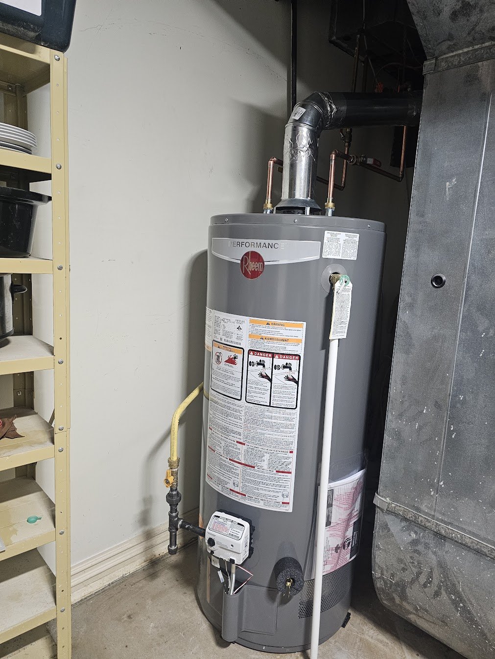A water heater in a utility closet with shelving on the left and an air duct on the right.