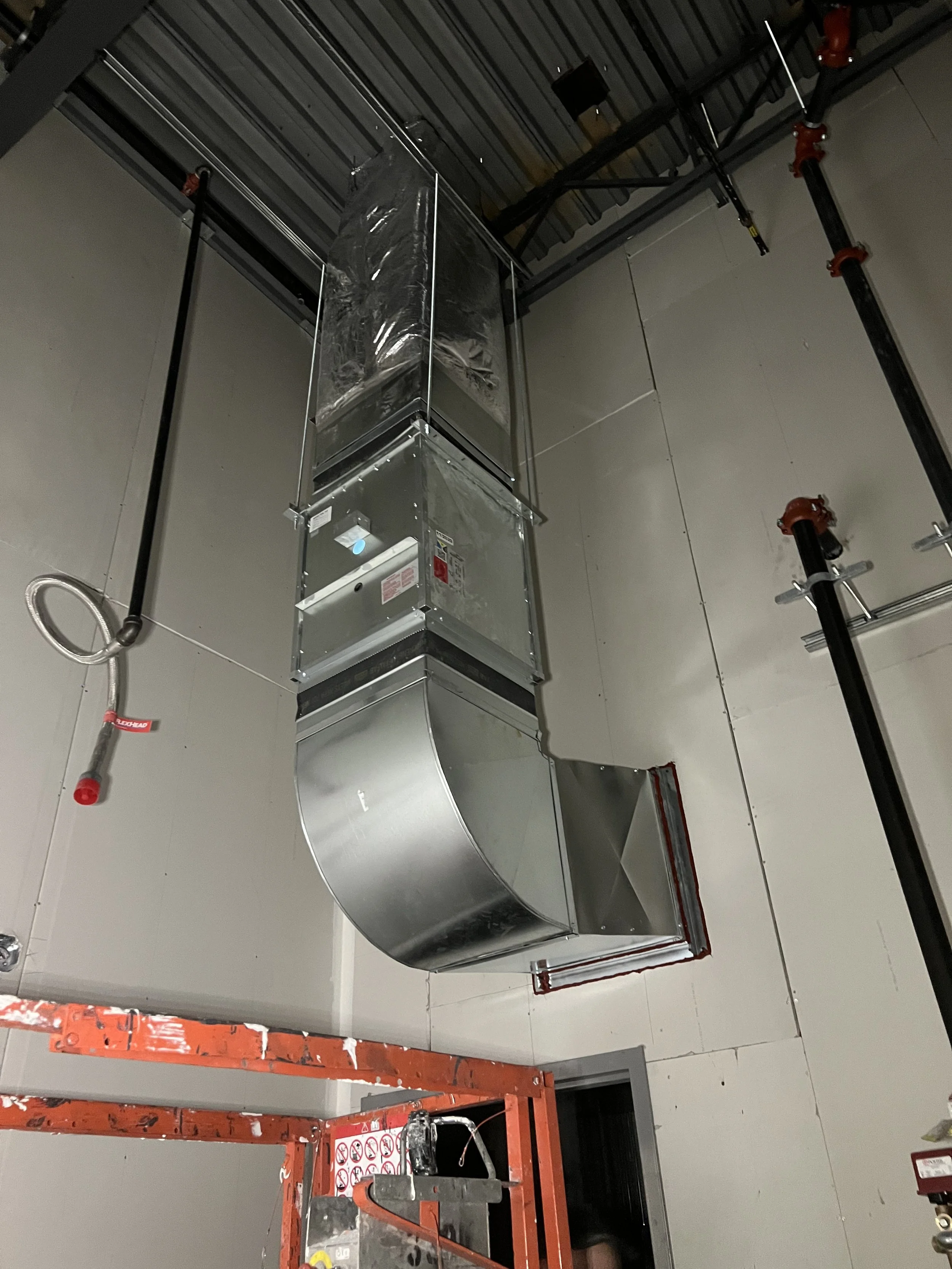 Construction workers installing a large, industrial ventilation ducting system in a building ceiling.