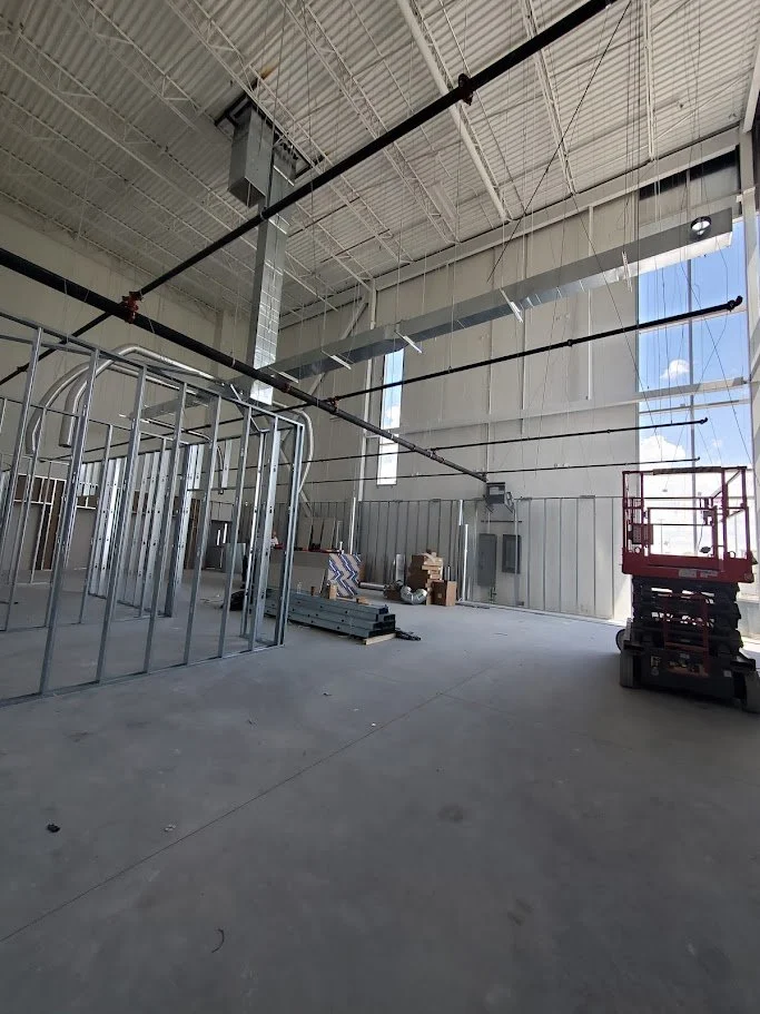 Interior of a warehouse or industrial space under construction with metal framing, construction materials, and a scissor lift.
