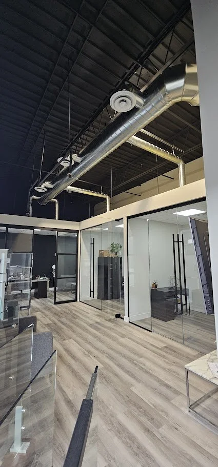 Modern office space with glass walls, exposed ductwork, and wooden flooring.