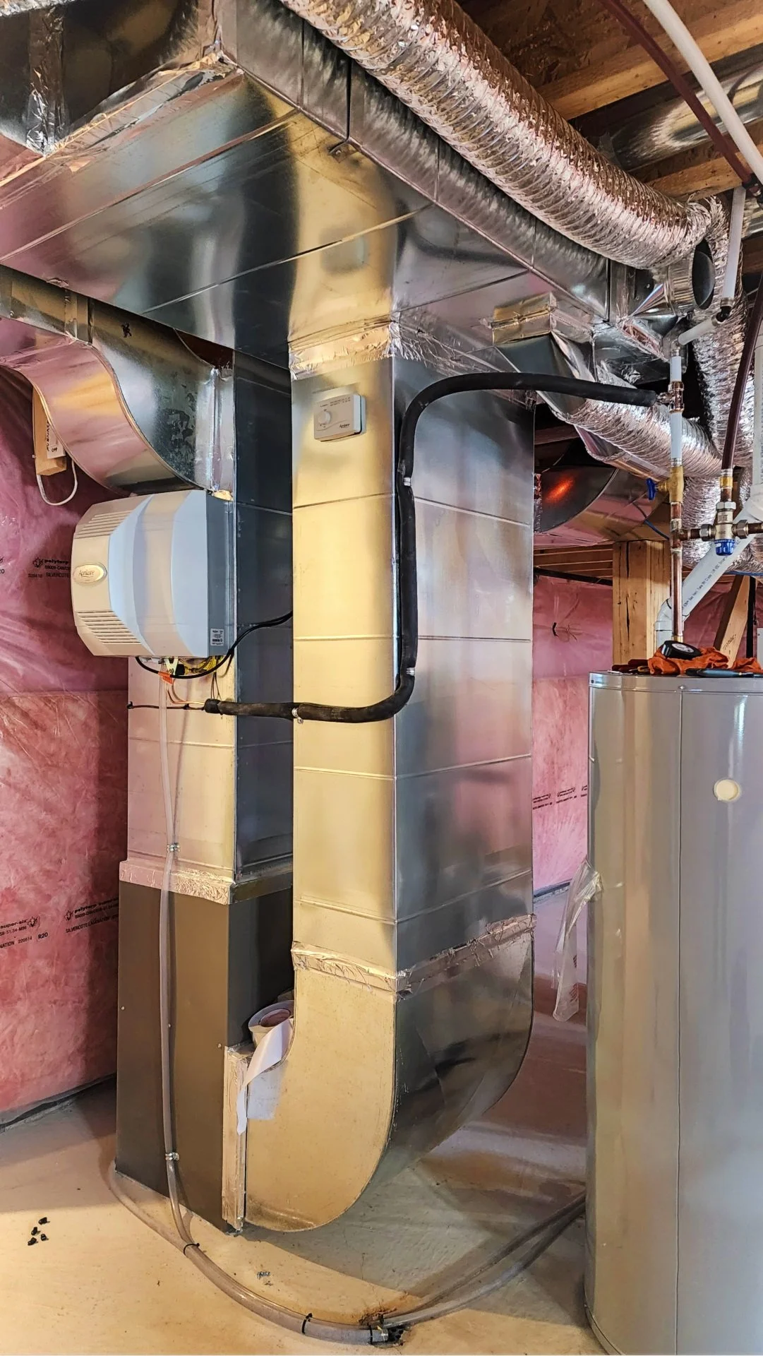 A view of a commercial HVAC system with ductwork, pipes, and insulation in a building under construction or renovation.