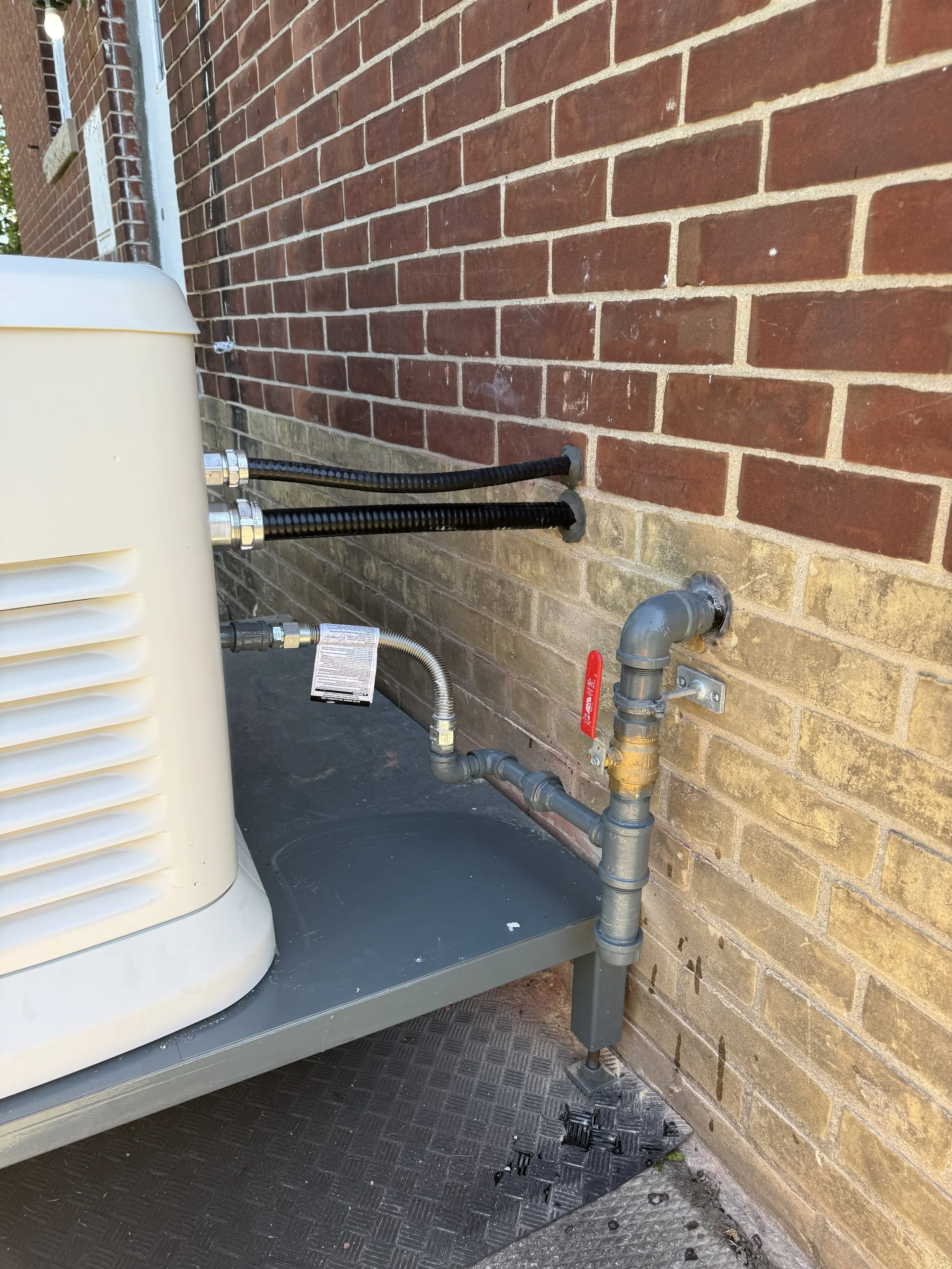 Outdoor HVAC unit connected to the building with pipes and hoses, against a brick wall.