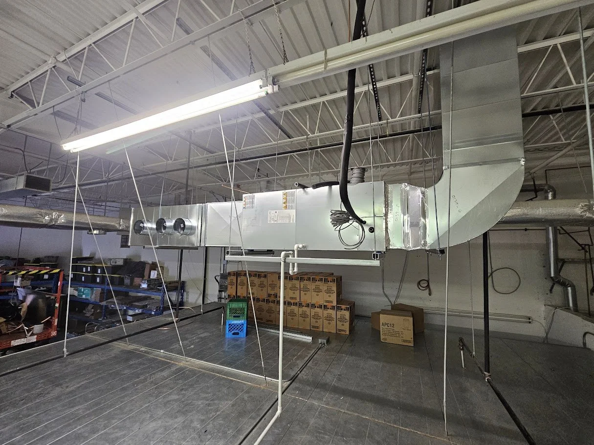Industrial ceiling with HVAC duct and fluorescent light fixture, shelves with boxes, and a raised black platform with a metal frame.