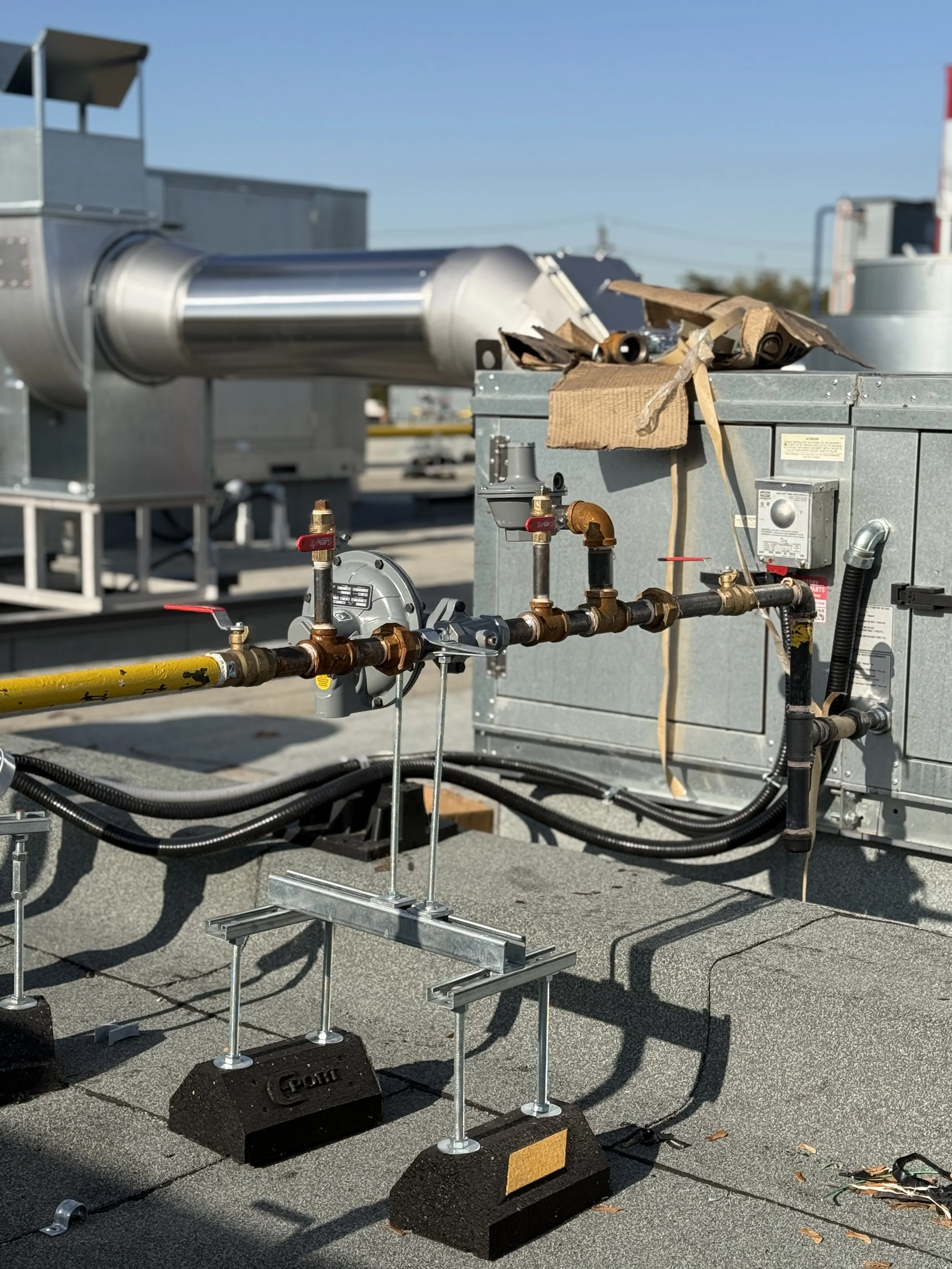 Mechanical equipment on a rooftop, including pipes, vents, and ductwork, with some cardboard and paper debris on top of the unit.