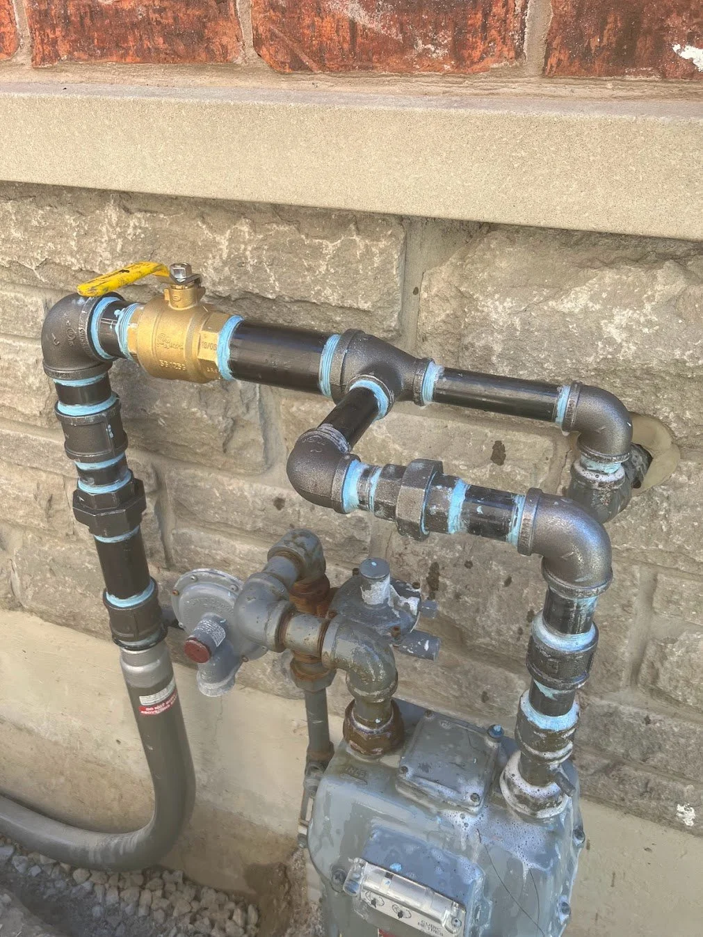 Plumbing pipes and a gas meter mounted on a brick wall.