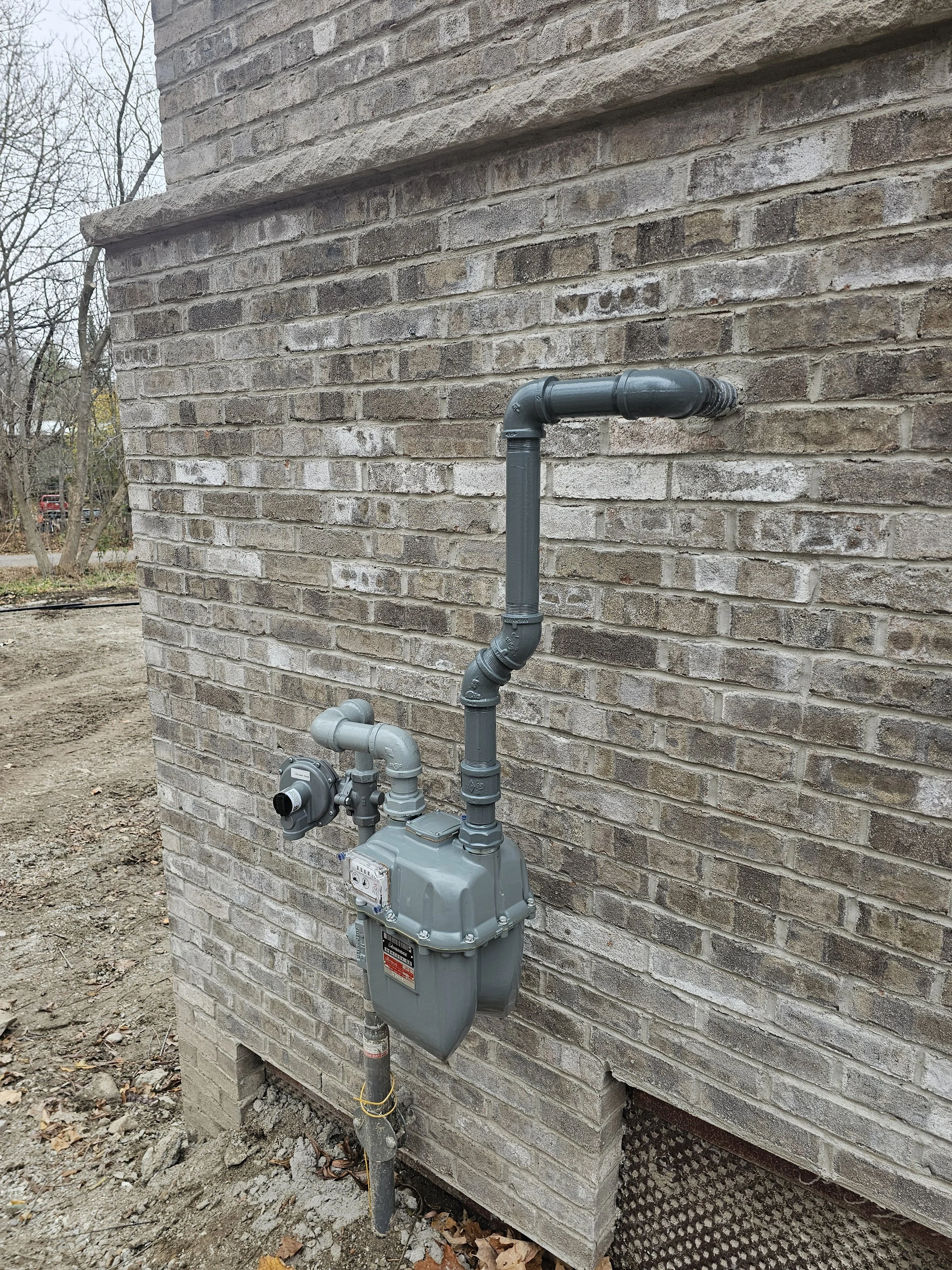 Gas meter and piping attached to an exterior brick wall of a building.