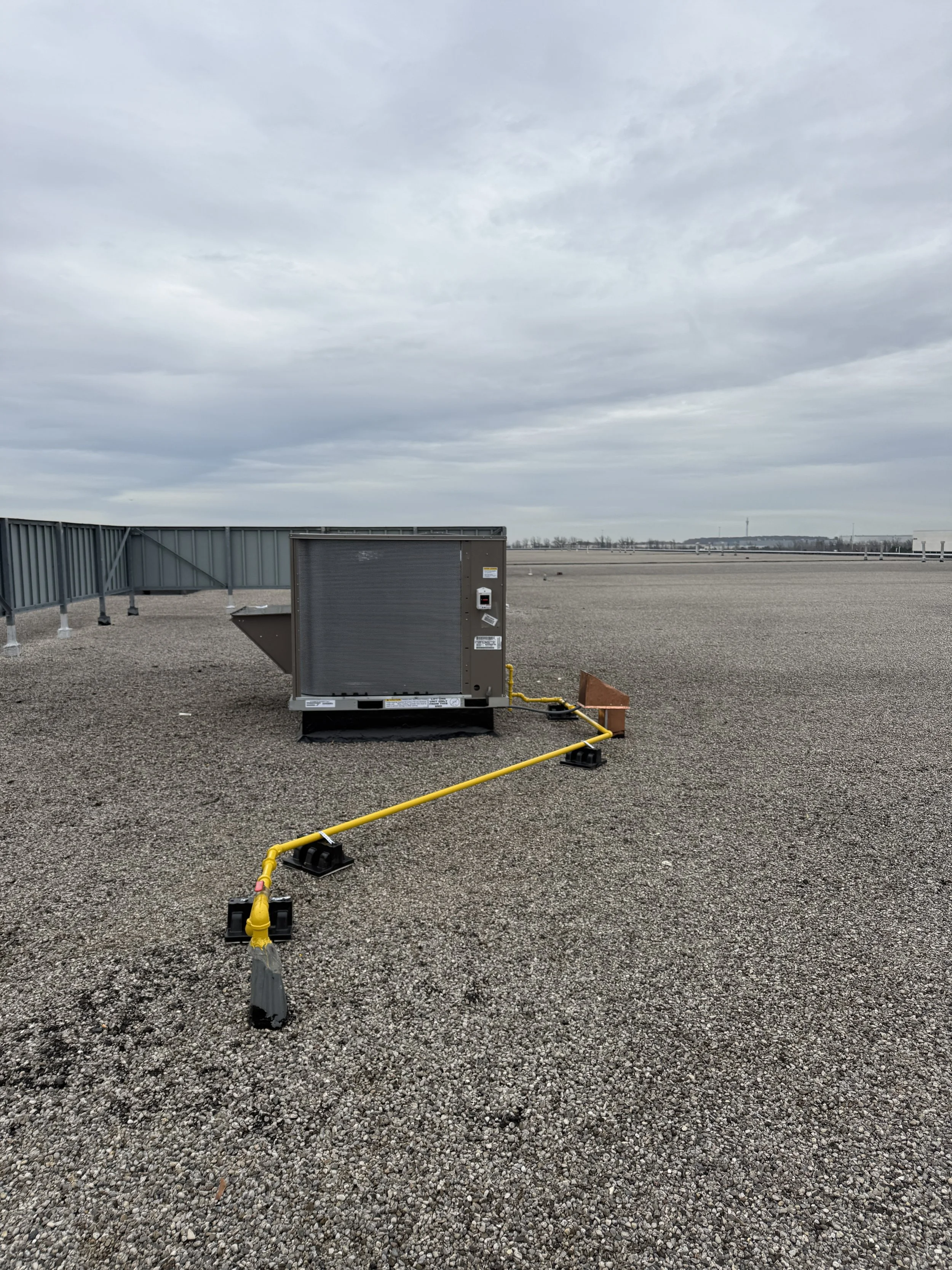 Rooftop HVAC unit on gravel surface with yellow gas line attached.