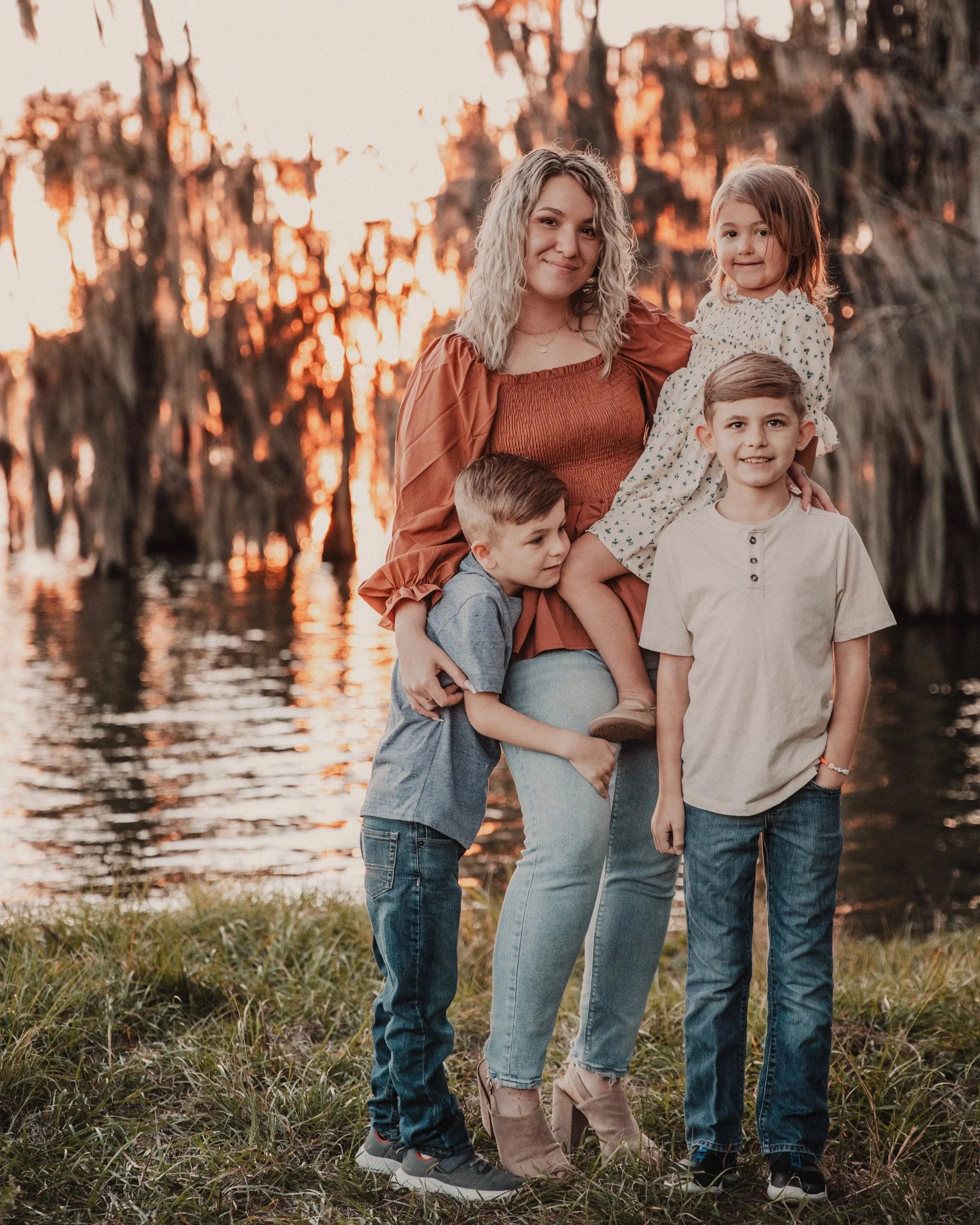 Paralegal Angela Roberts with her three children standing outdoors near water at sunset, smiling, with trees in the background.