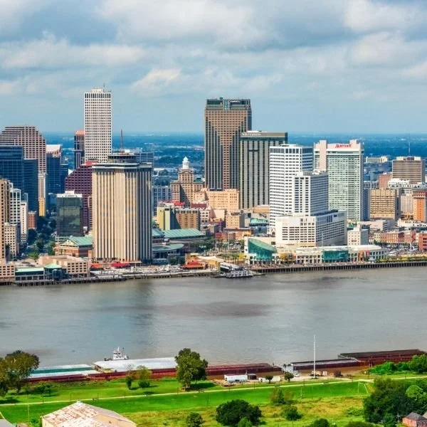 Aerial view of a city skyline with high-rise buildings along a river, green park area in the foreground, and a partly cloudy sky.