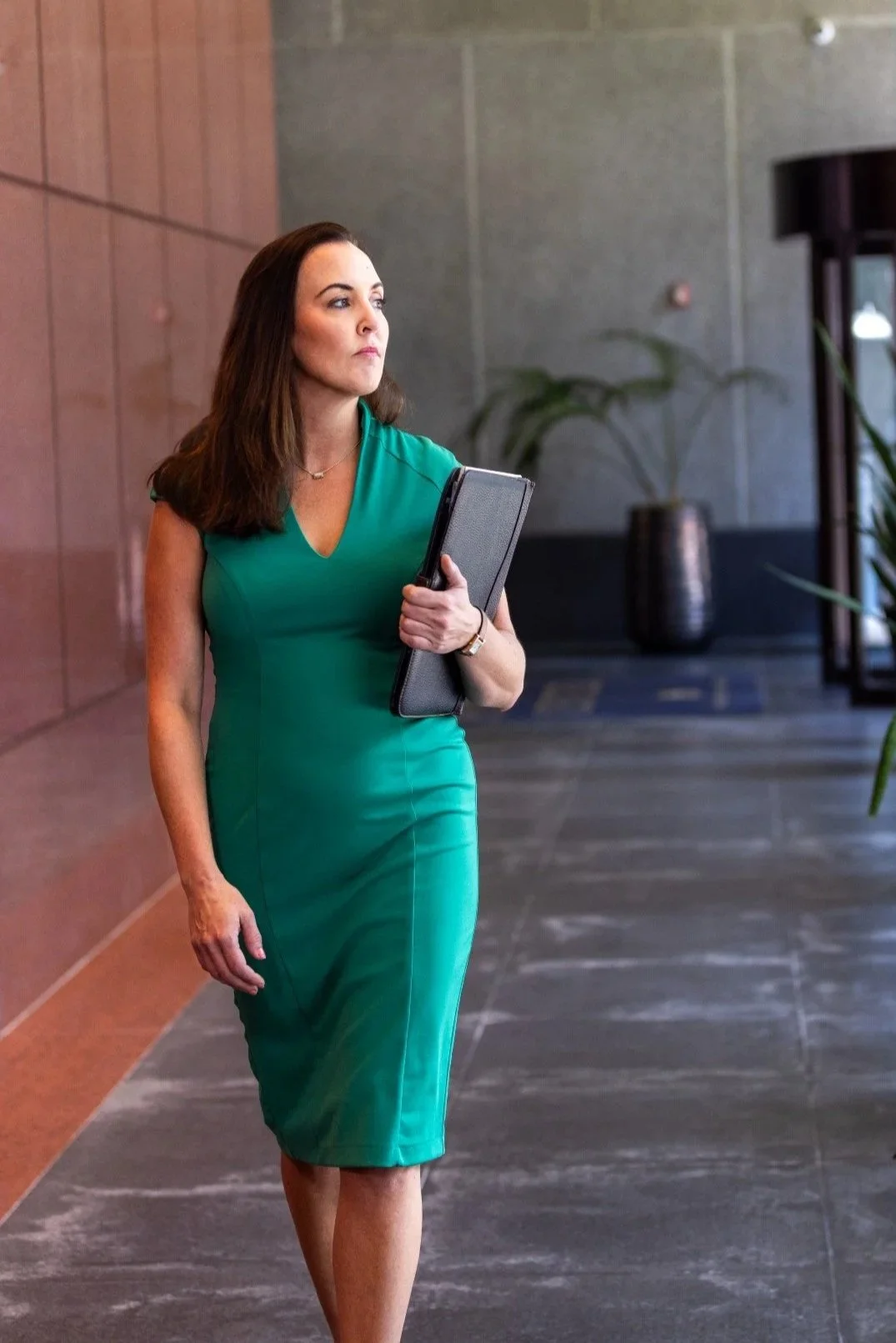 Attorney Lindsey Cheek in a teal dress holding a folder walking in a modern office lobby.