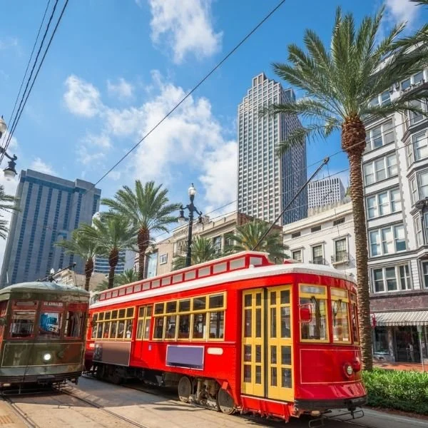 A historic red streetcar with yellow door and window frames on a street in downtown, surrounded by palm trees, modern tall buildings, and a clear blue sky.