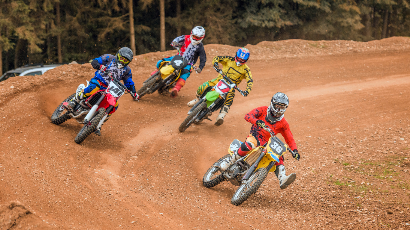 Five motocross riders racing on a dirt track, wearing colorful gear and helmets, navigating a curve.