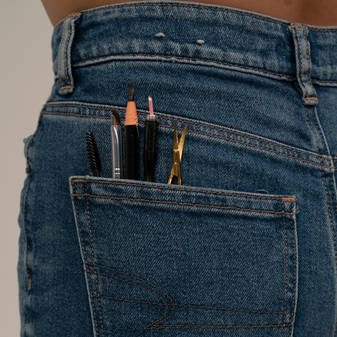 Back pocket of blue denim jeans containing various tools, including a wire brush, cutting tools, tweezers, and a small spatula.