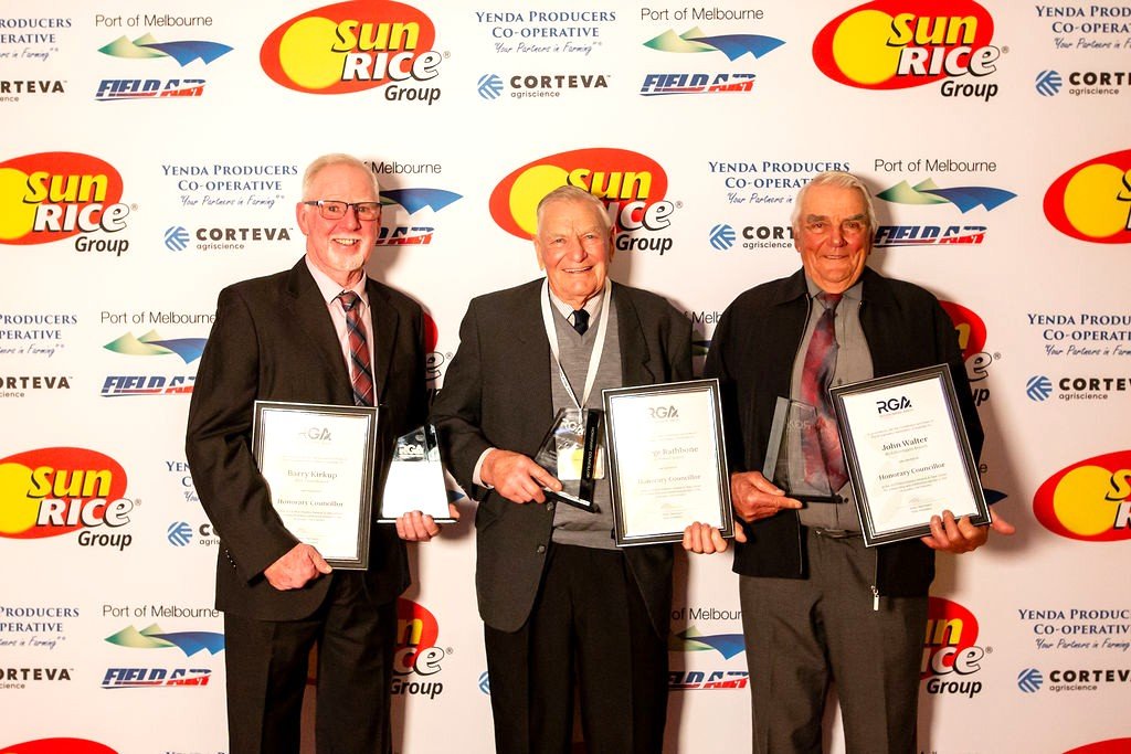 Three men in suits holding framed awards and trophies, standing in front of a backdrop with logos including Sun Rice Group, Yenda Producers Co-operative, Port of Melbourne, and others at an award ceremony.