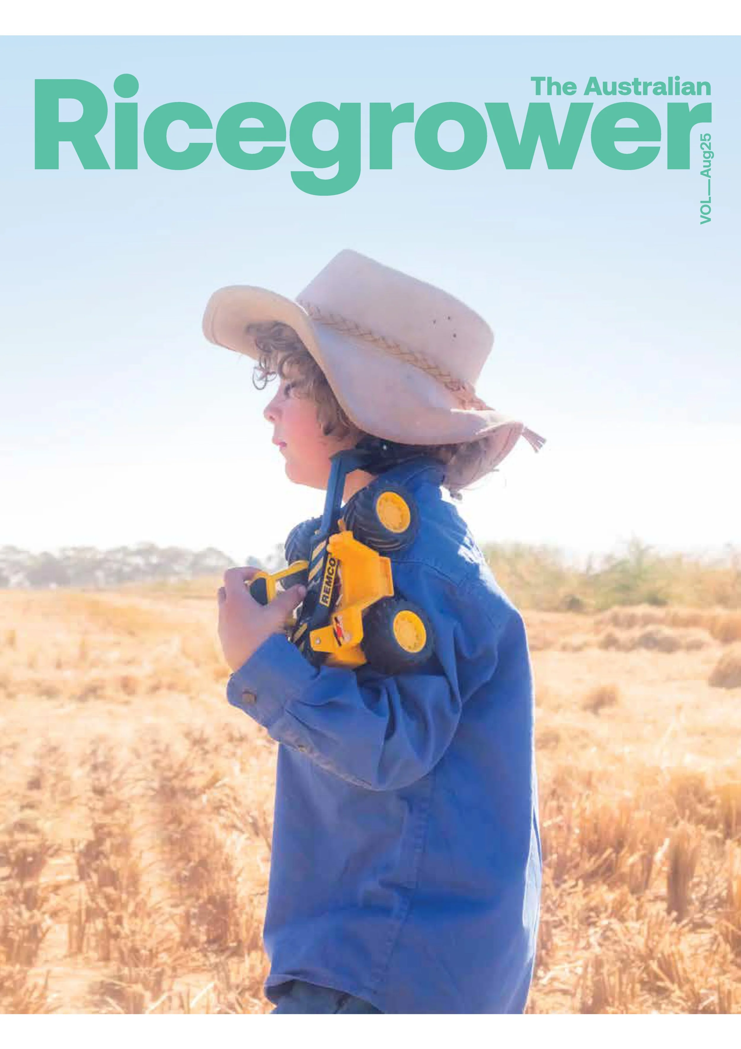 Cover of The Australian Ricegrower magazine, August 2025 issue, featuring a young child in a blue jacket and wide-brimmed hat standing in a field with a toy construction vehicle over their shoulder.