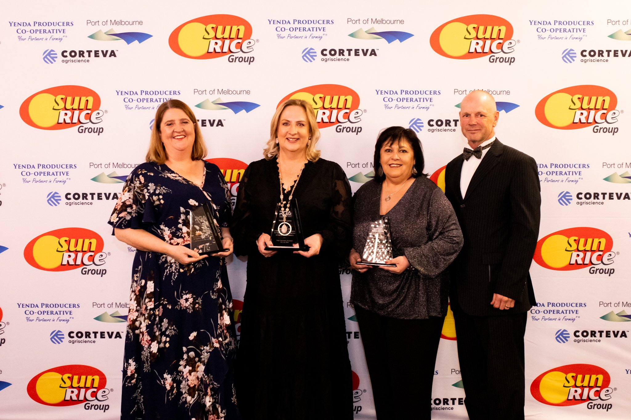 Four people standing in front of a backdrop with Sun Rice Group, Corteva agriscience, and Port of Melbourne logos, holding awards, dressed in formal attire, smiling at the camera.