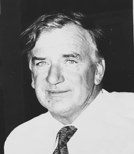 Black and white portrait of a middle-aged man with dark hair, wearing a white shirt and patterned tie.